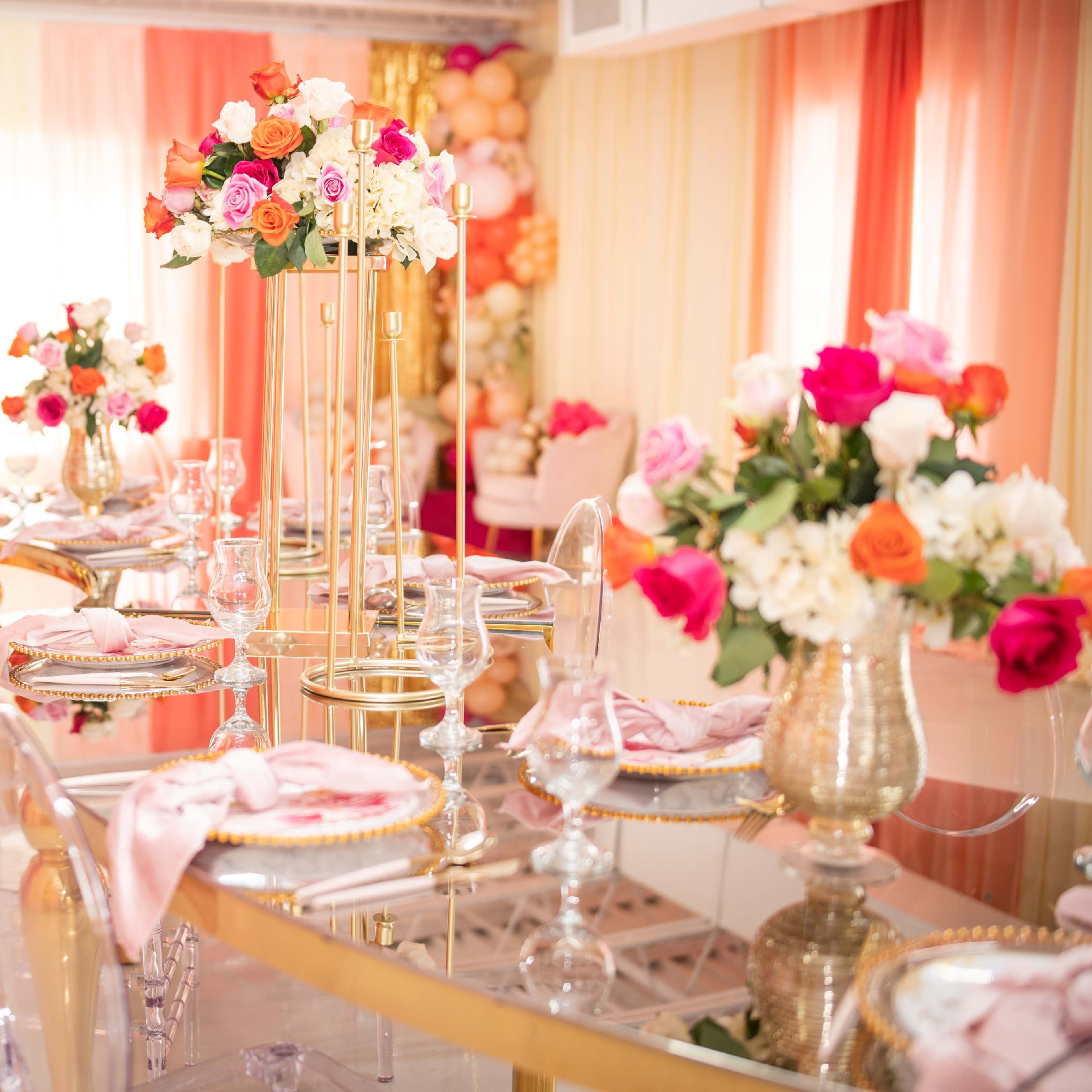 A dining area is set with elegant tables adorned with floral centerpieces and a backdrop of colorful balloons.