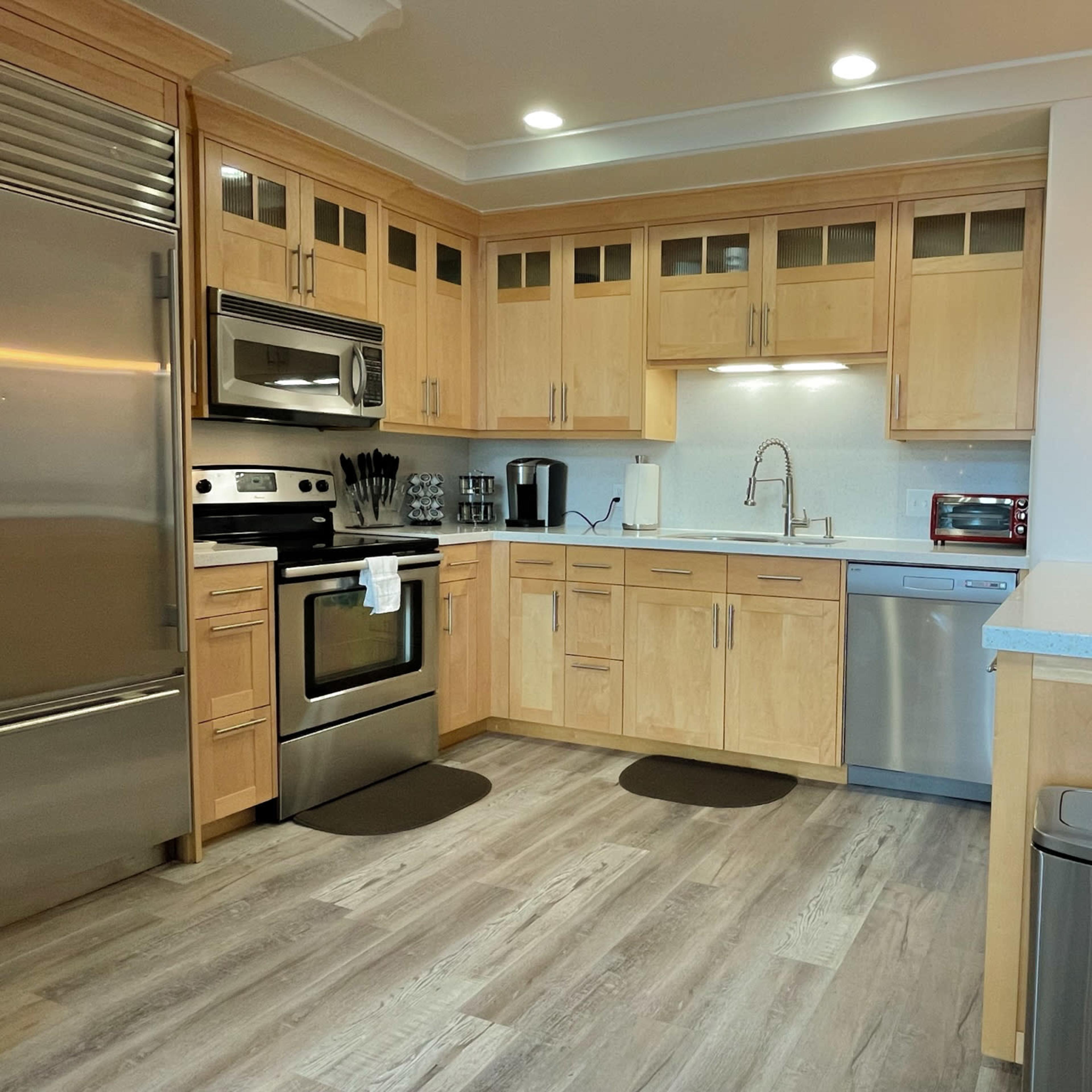 A modern kitchen with wooden cabinets, stainless steel appliances, and a countertop with bar seating.