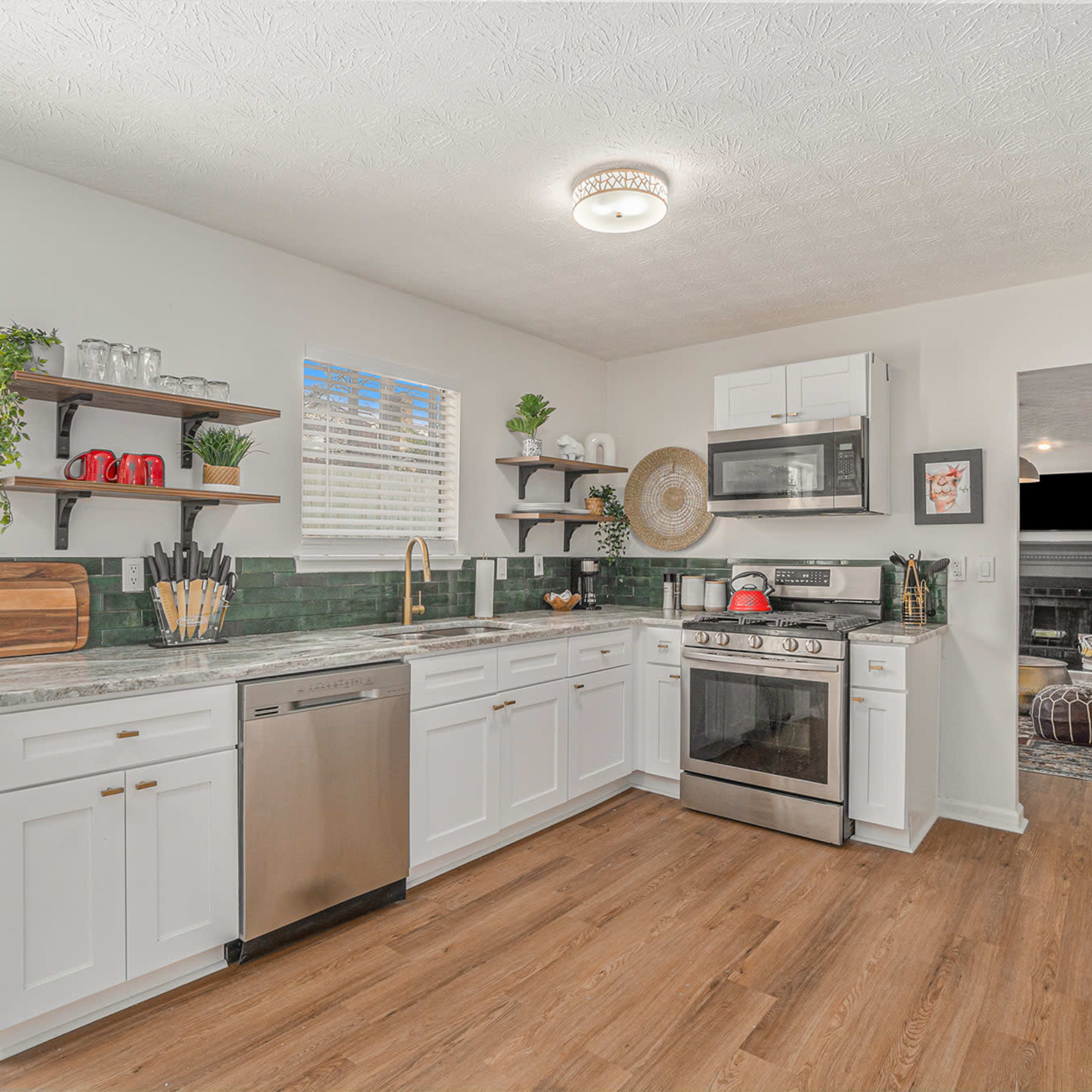 A modern kitchen features white cabinetry, stainless steel appliances, and a green tile backsplash, with a dining area visible in the background.