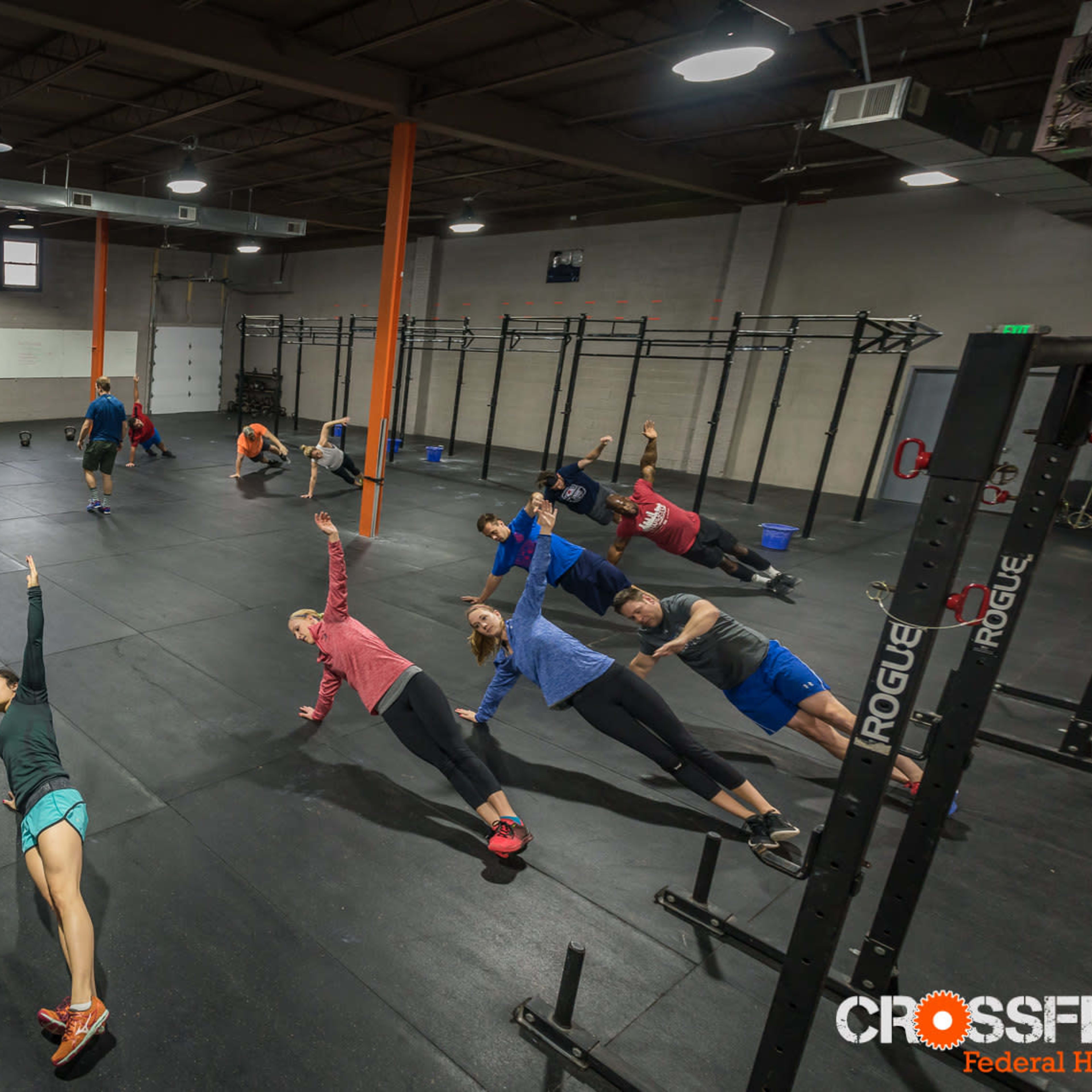 A group of people is performing a fitness routine on gym mats in a CrossFit facility.