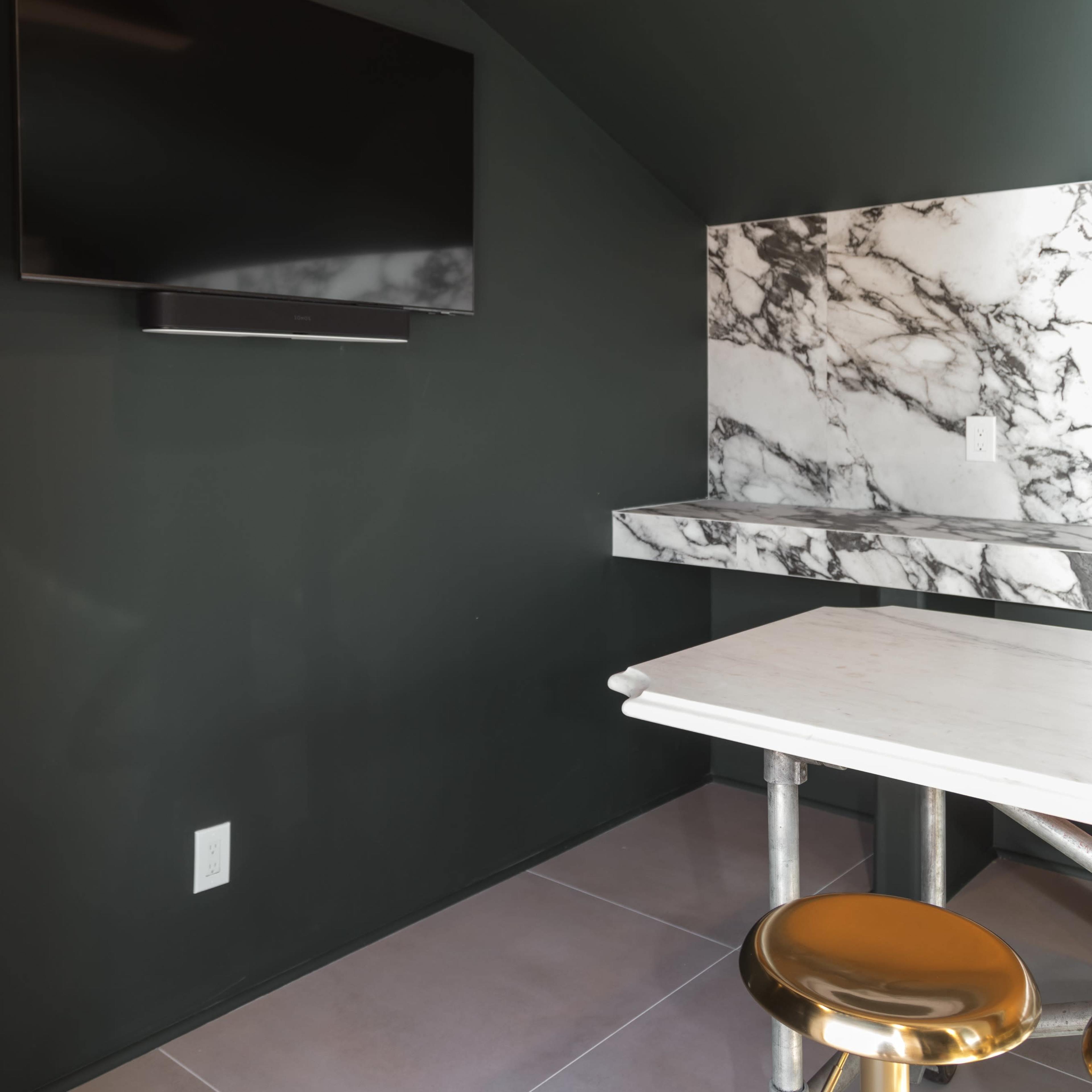 A small room featuring a marble wall, a mounted television, and a table with metallic legs.