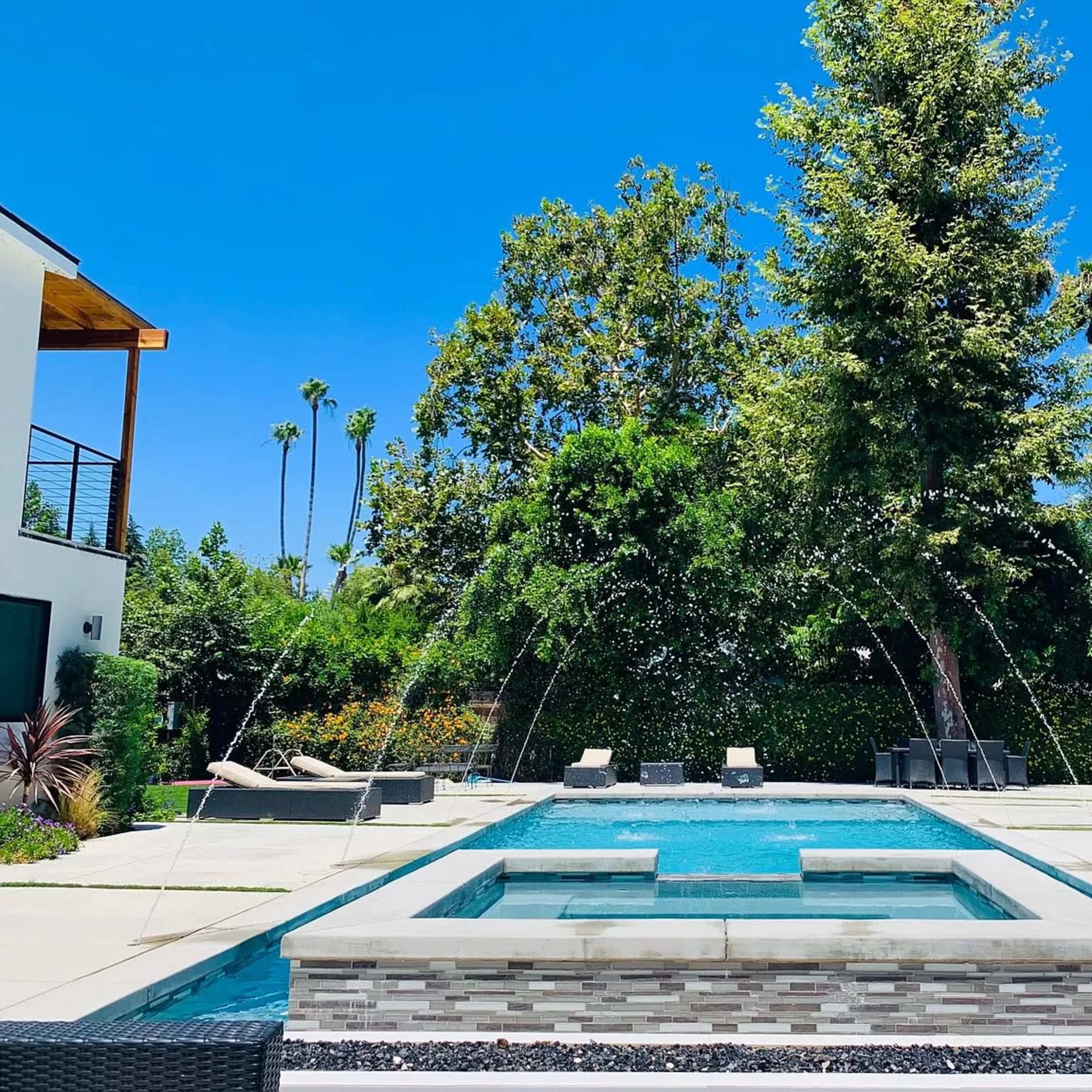 A modern pool surrounded by lush greenery and sun loungers under a clear blue sky.