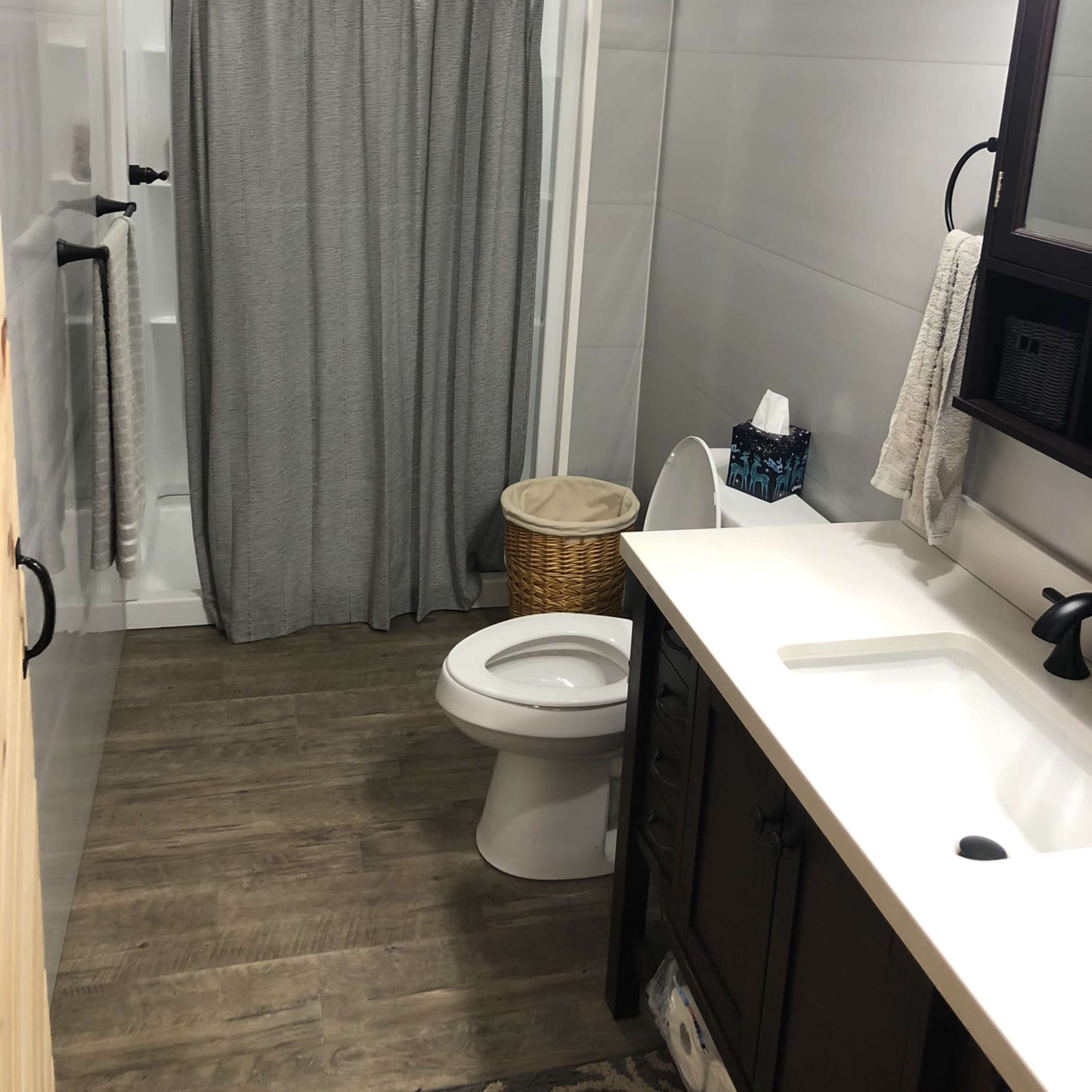 A modern bathroom featuring a shower with a gray curtain, a toilet, a sink with dark cabinetry, and a laundry basket.