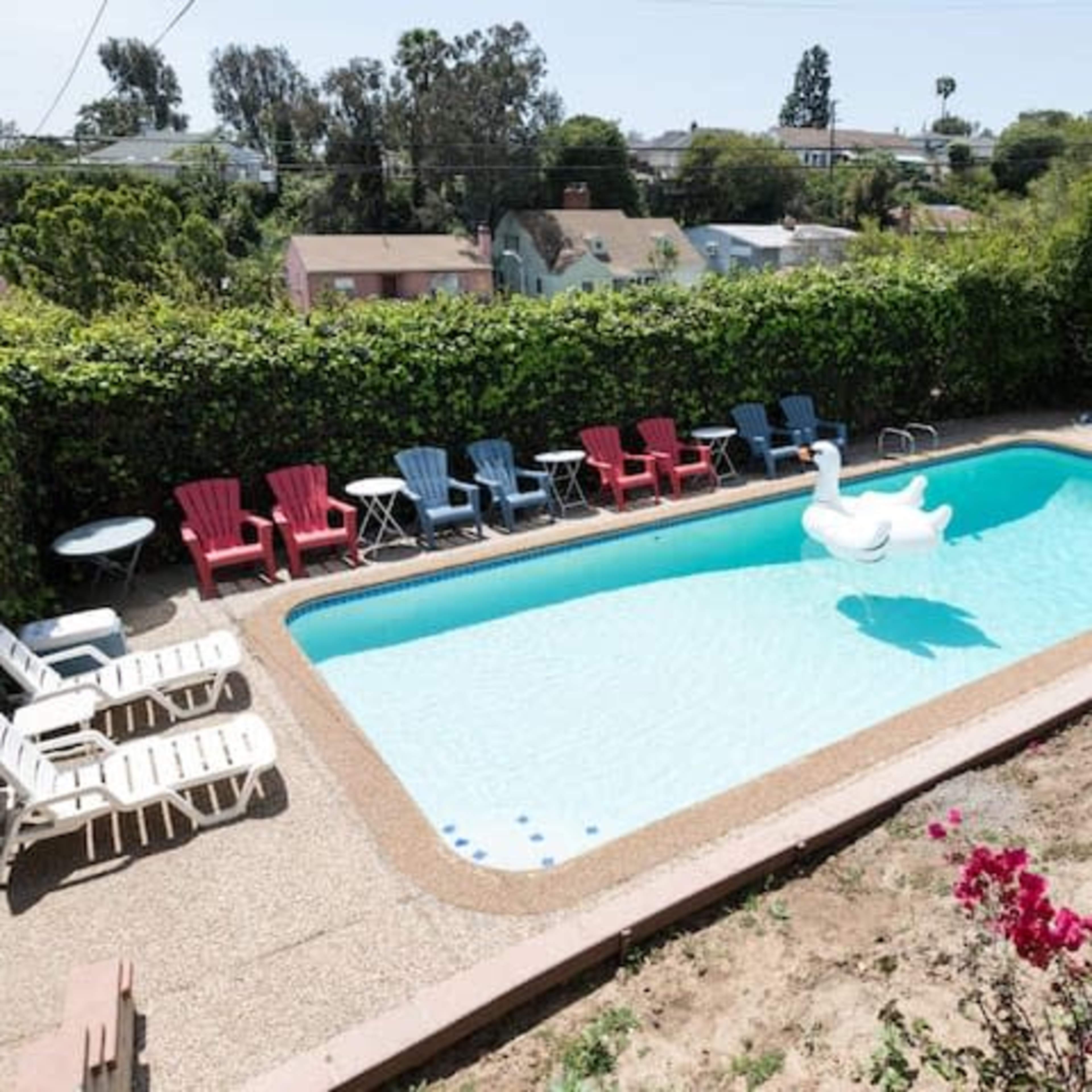 A rectangular swimming pool surrounded by lounge chairs of various colors and a large inflatable swan floats on the water.