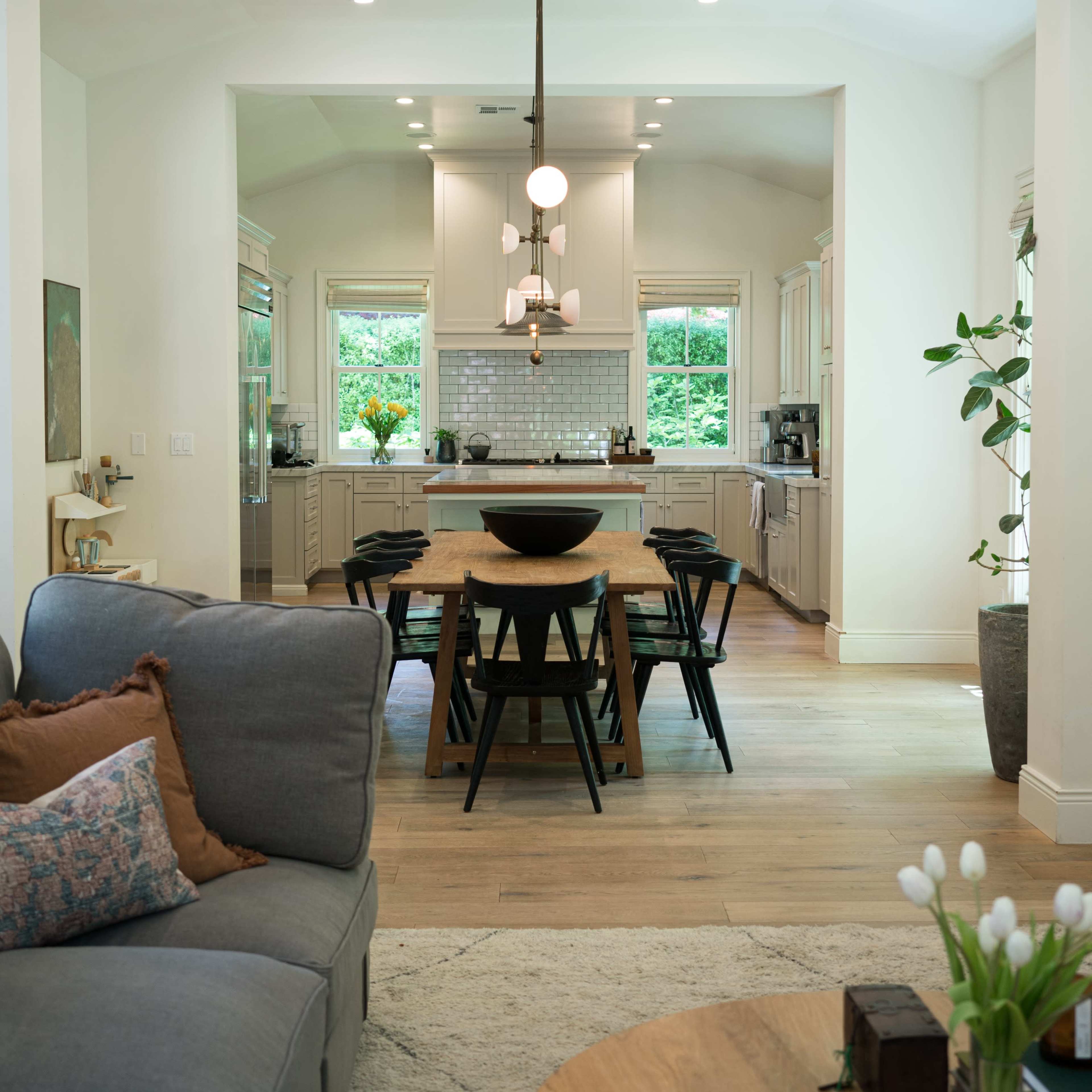 A modern, open-concept kitchen and dining area with a large table, stylish light fixture, and soft seating.