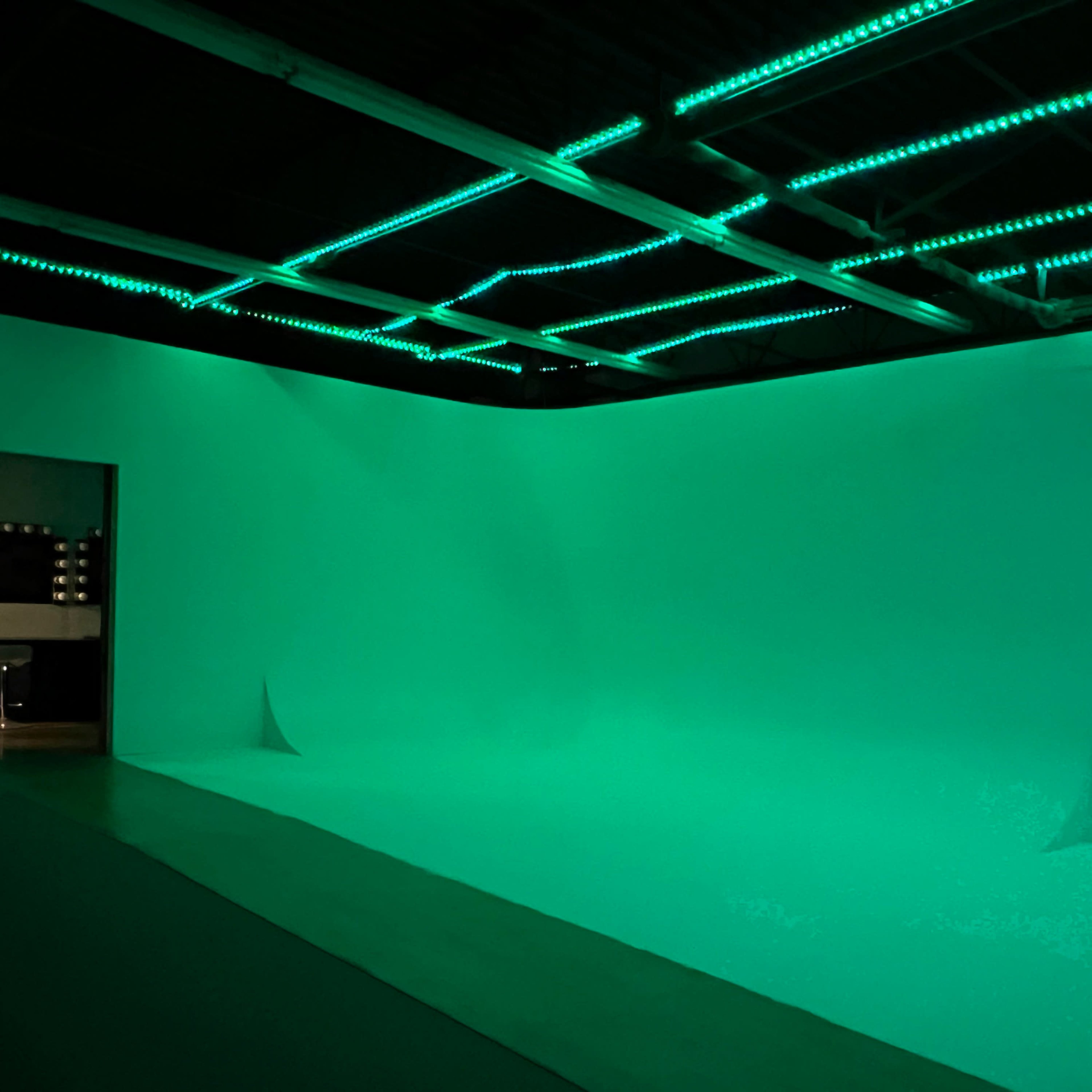A studio space features a green backdrop and illuminated ceiling lights, creating a uniform color effect.