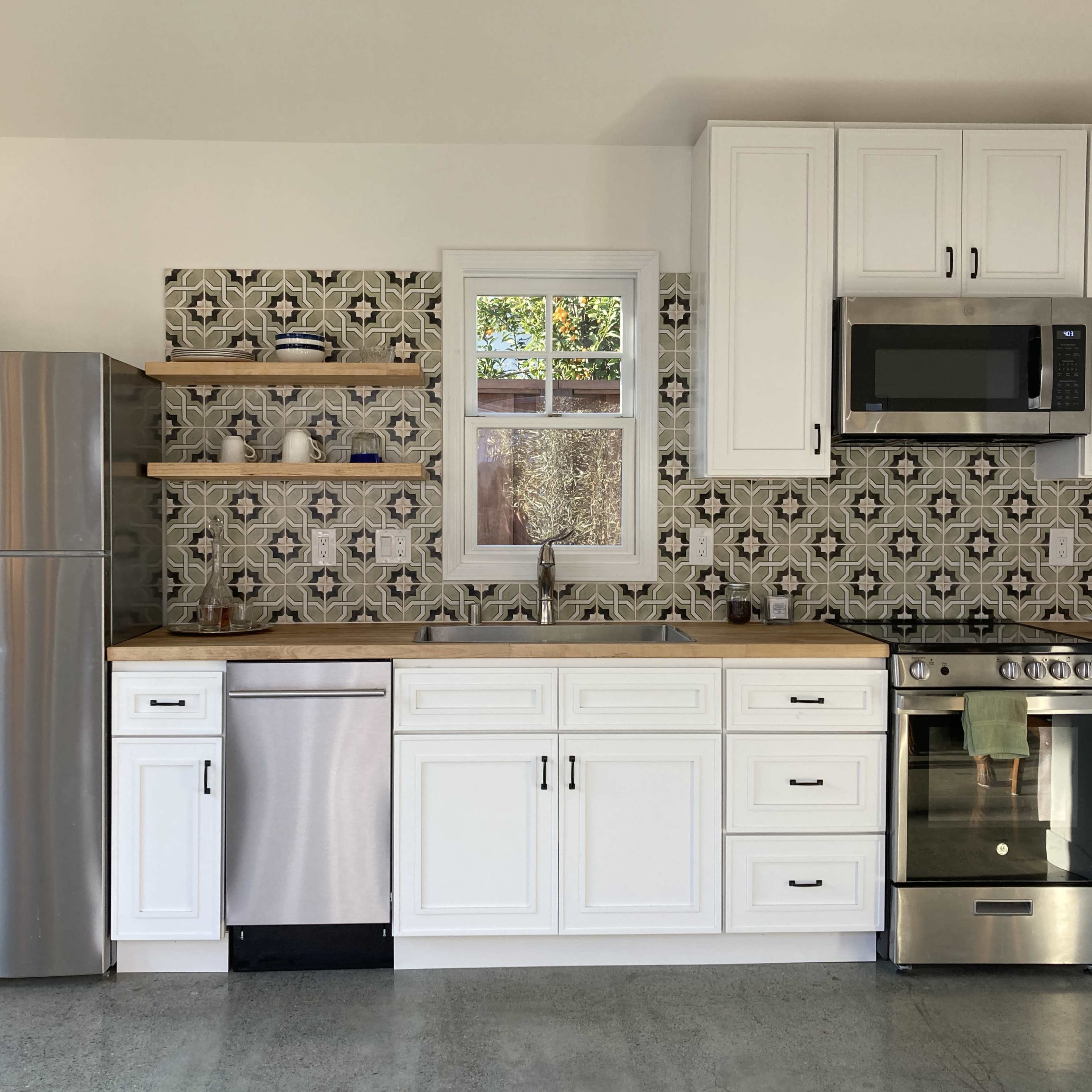 A modern kitchen with white cabinets, stainless steel appliances, and patterned backsplash tiles.