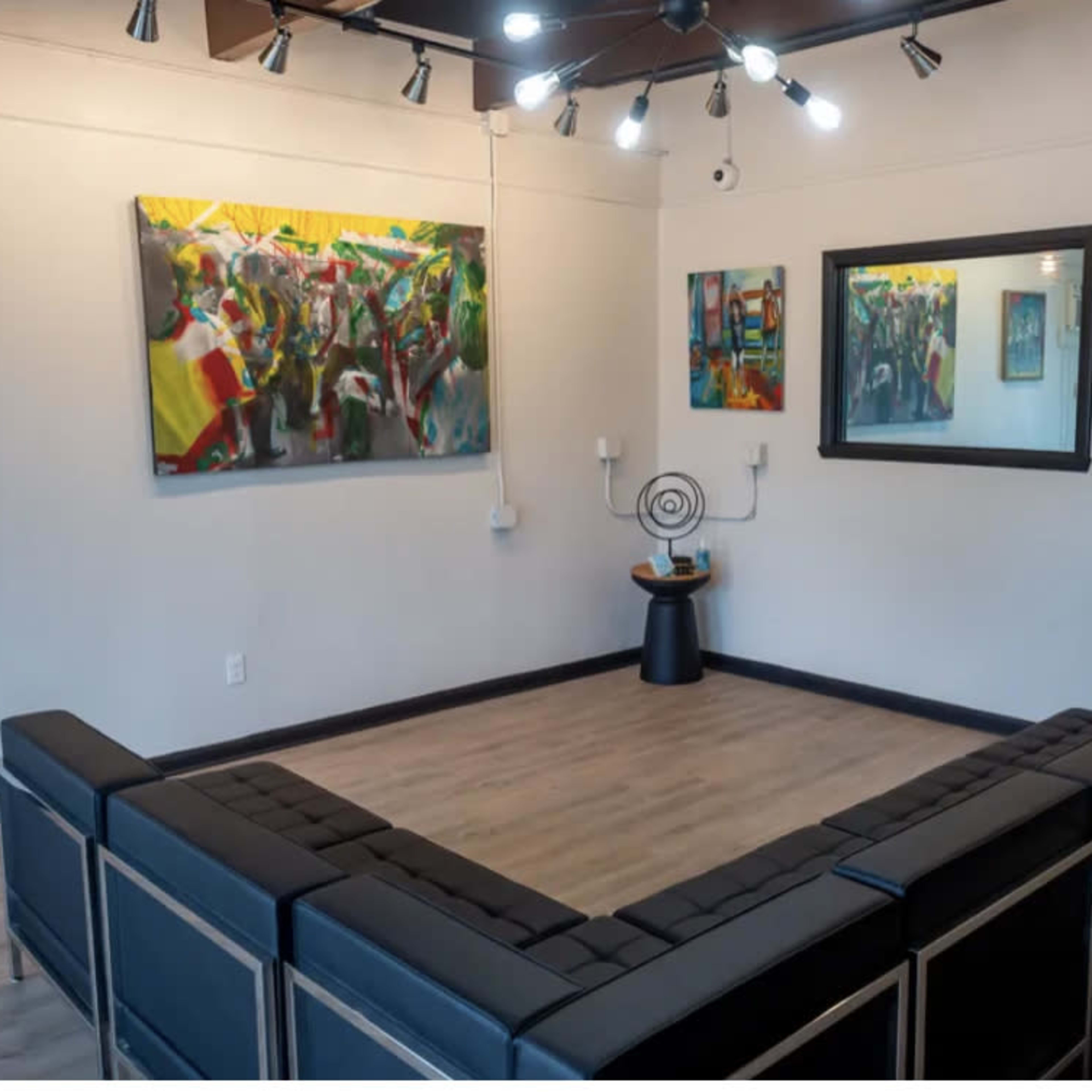A modern art gallery with a U-shaped seating arrangement facing colorful paintings on the walls and a round decorative piece in the center.