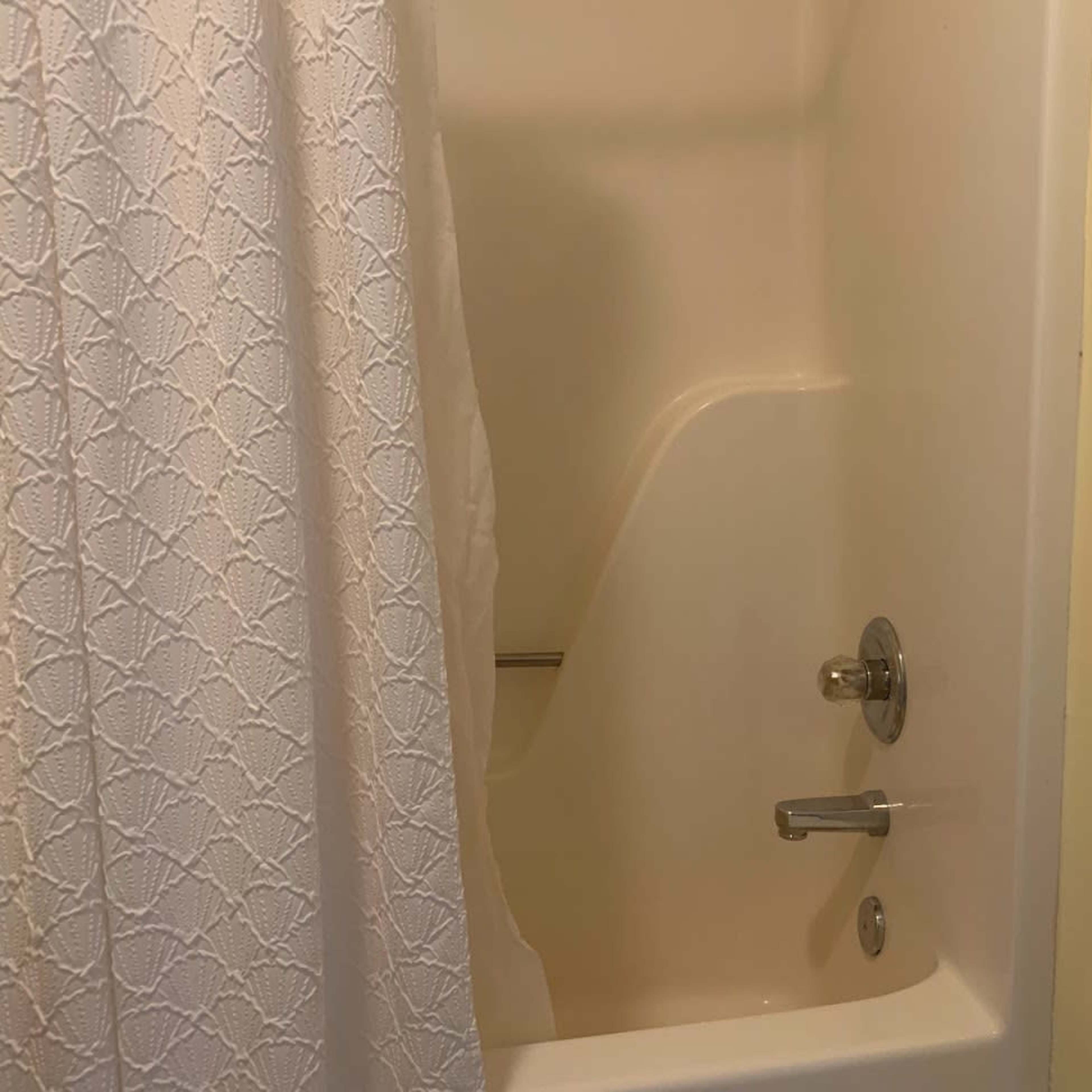 A small bathroom features a shower with a white curtain and a tub.