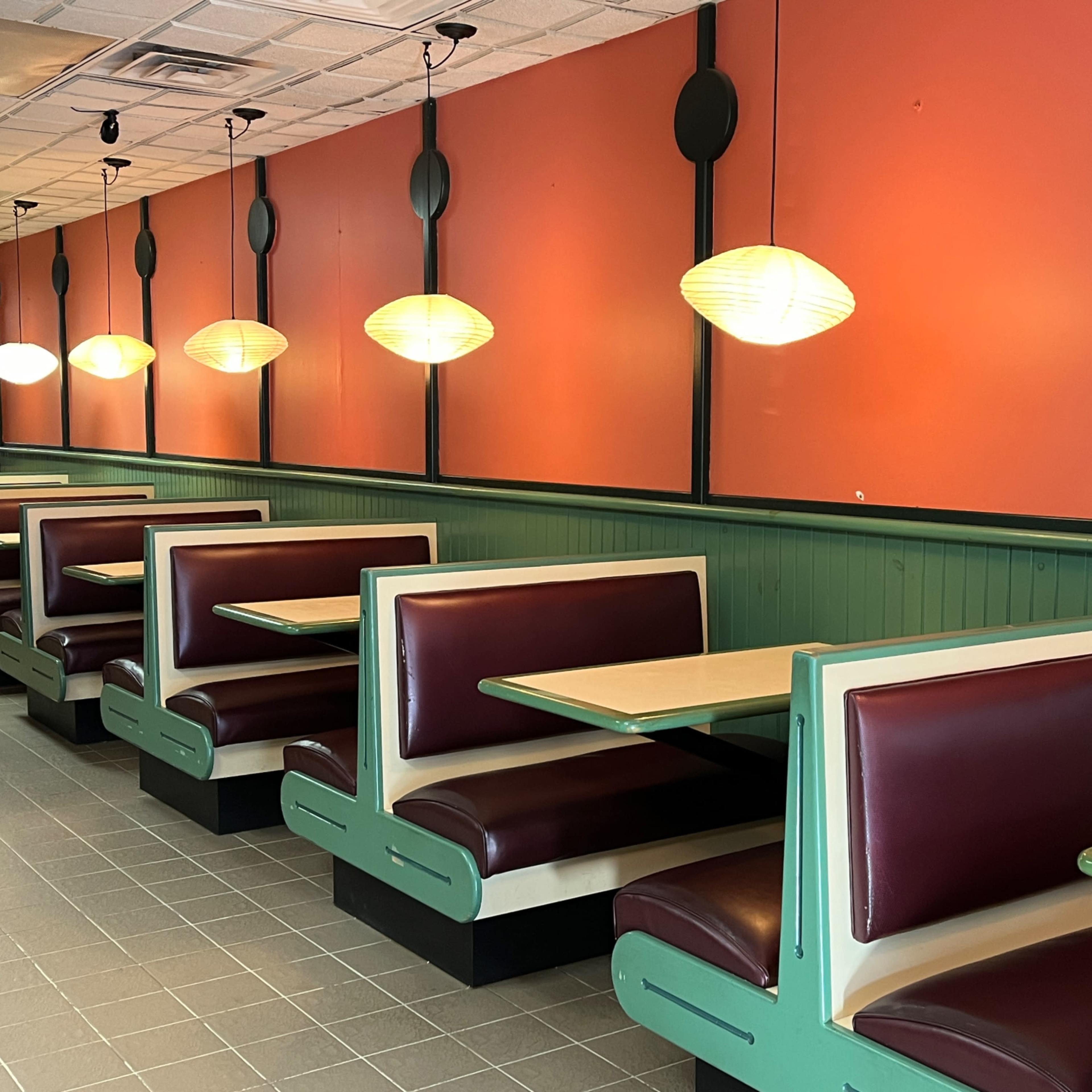 A diner interior with red walls, green paneling, and several booths arranged along the space, illuminated by hanging pendant lights.