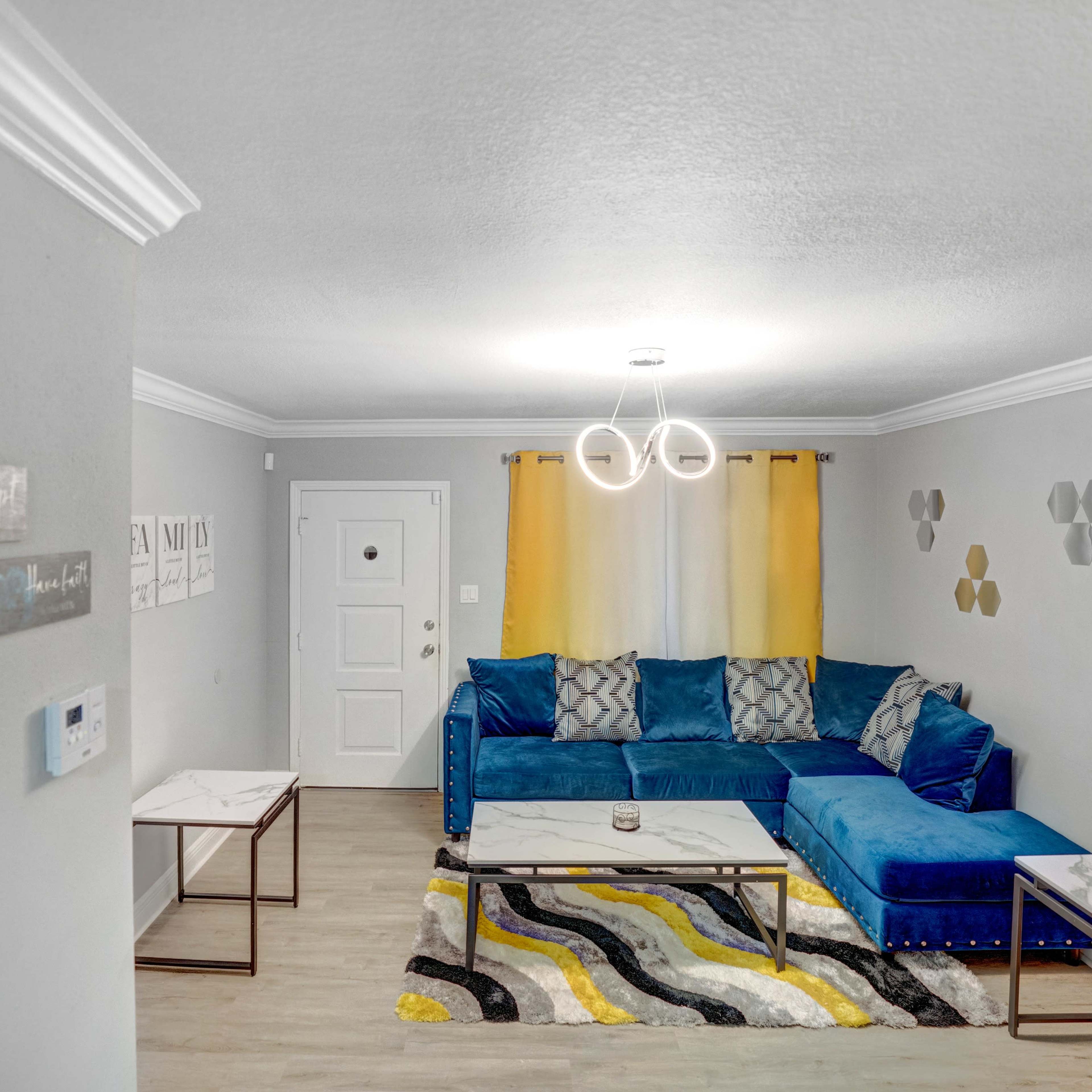 A modern living room with a blue sectional sofa, two marble-top coffee tables, and yellow curtains beside a white door.