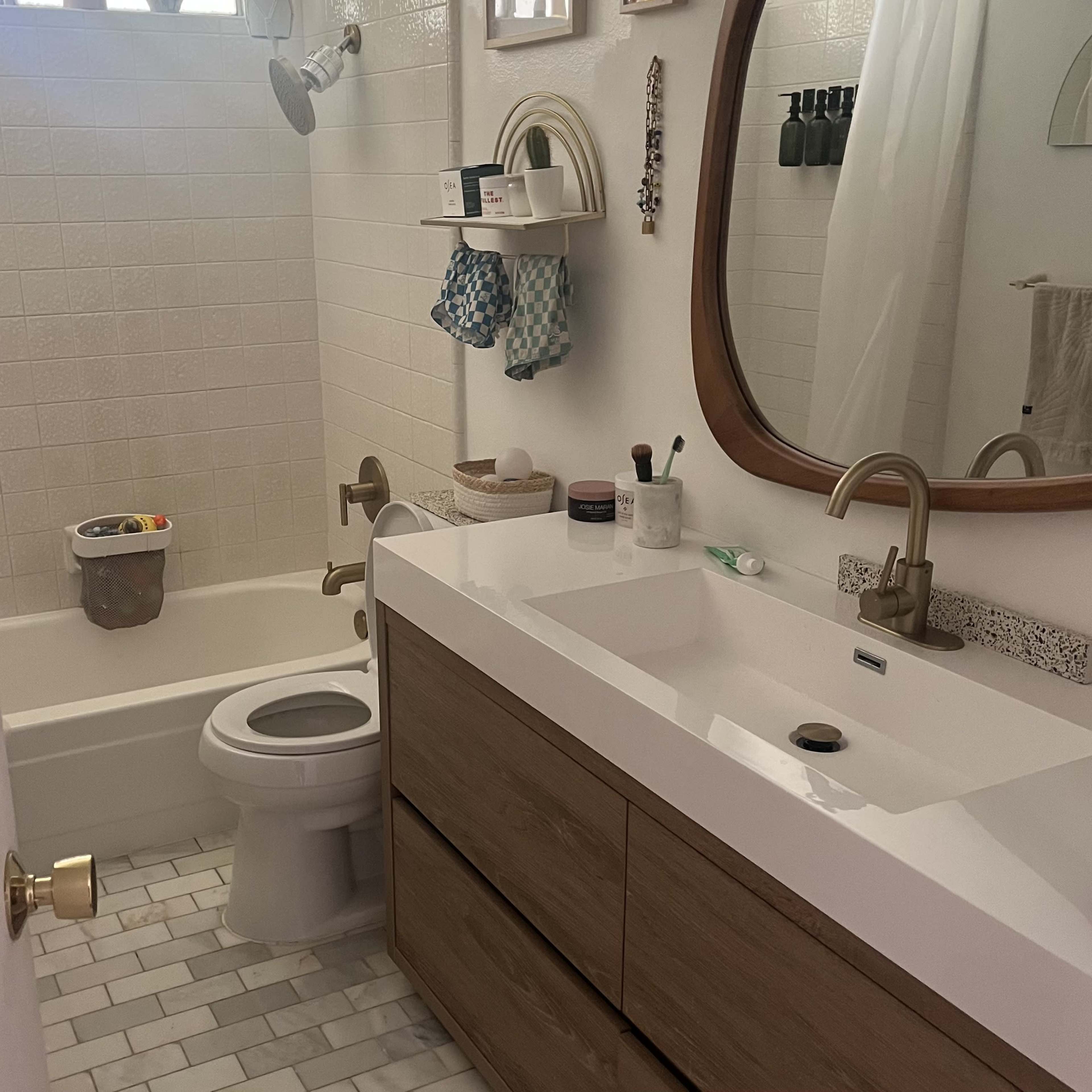 A modern bathroom with a bathtub, a toilet, a wooden vanity with a sink, and a mirror above the vanity.