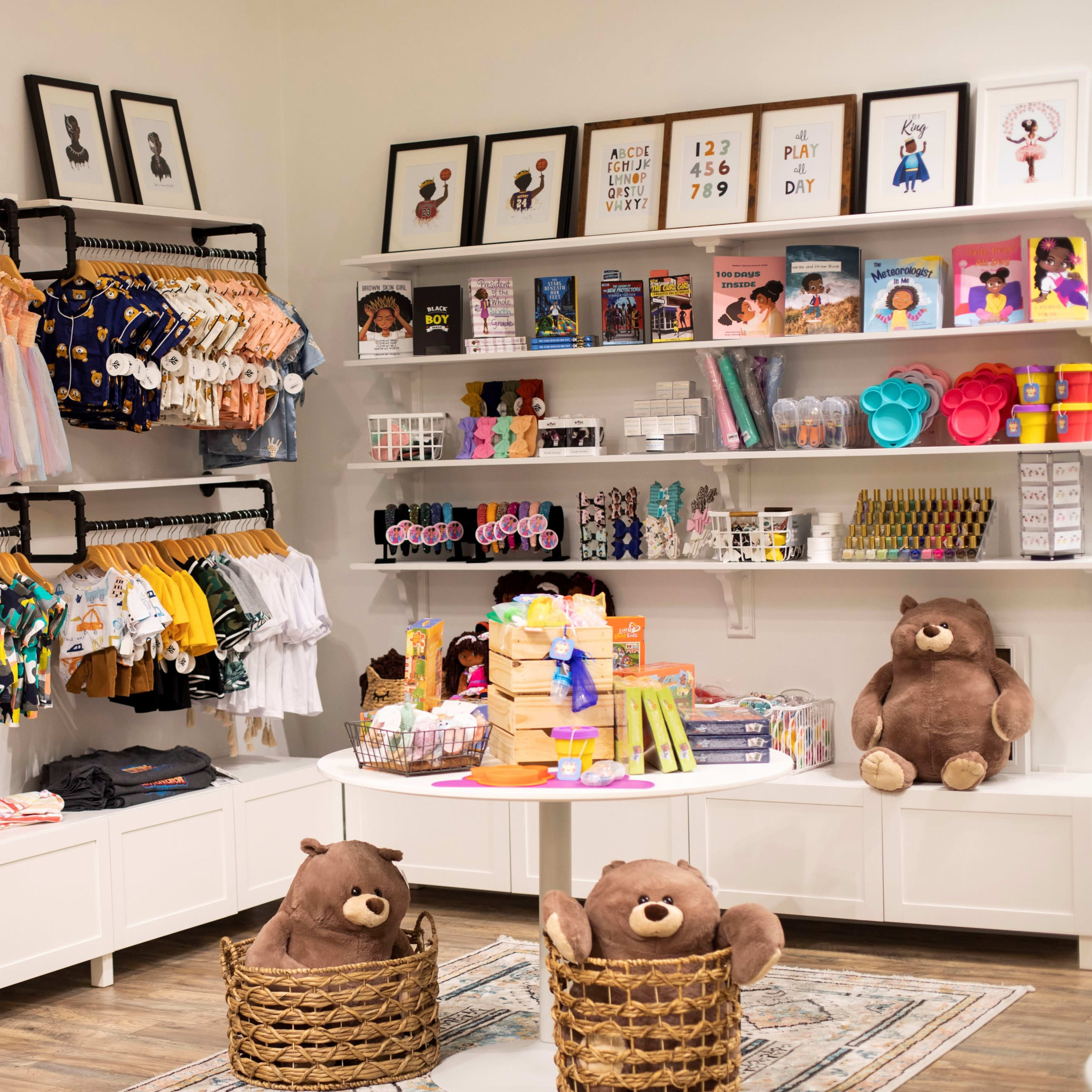 A brightly lit children's clothing and toy store featuring colorful clothing on hangers, books, and stuffed animals displayed on shelves and tables.
