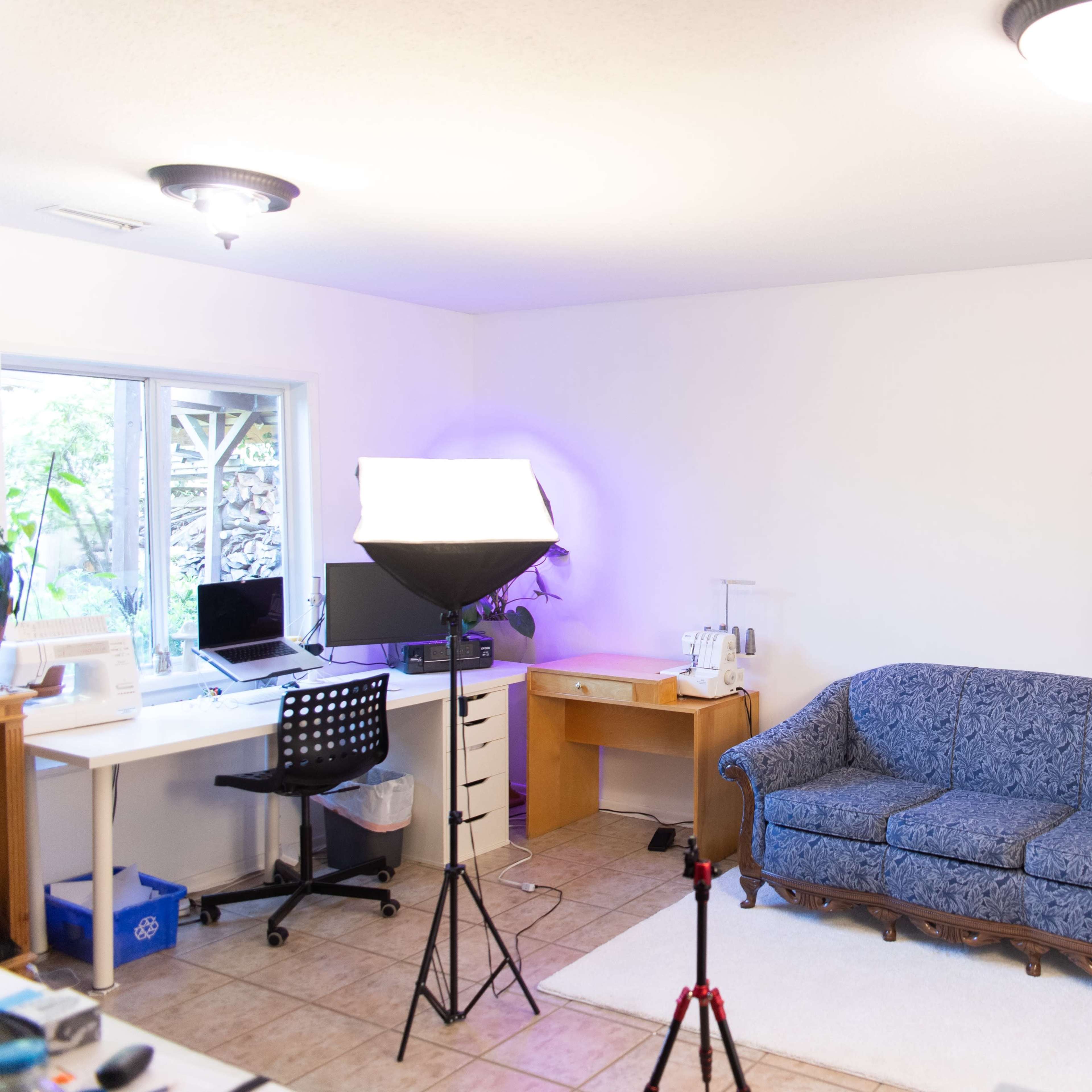 A well-lit, uncluttered room with a blue couch, a desk with a computer, and photography lighting equipment set up.
