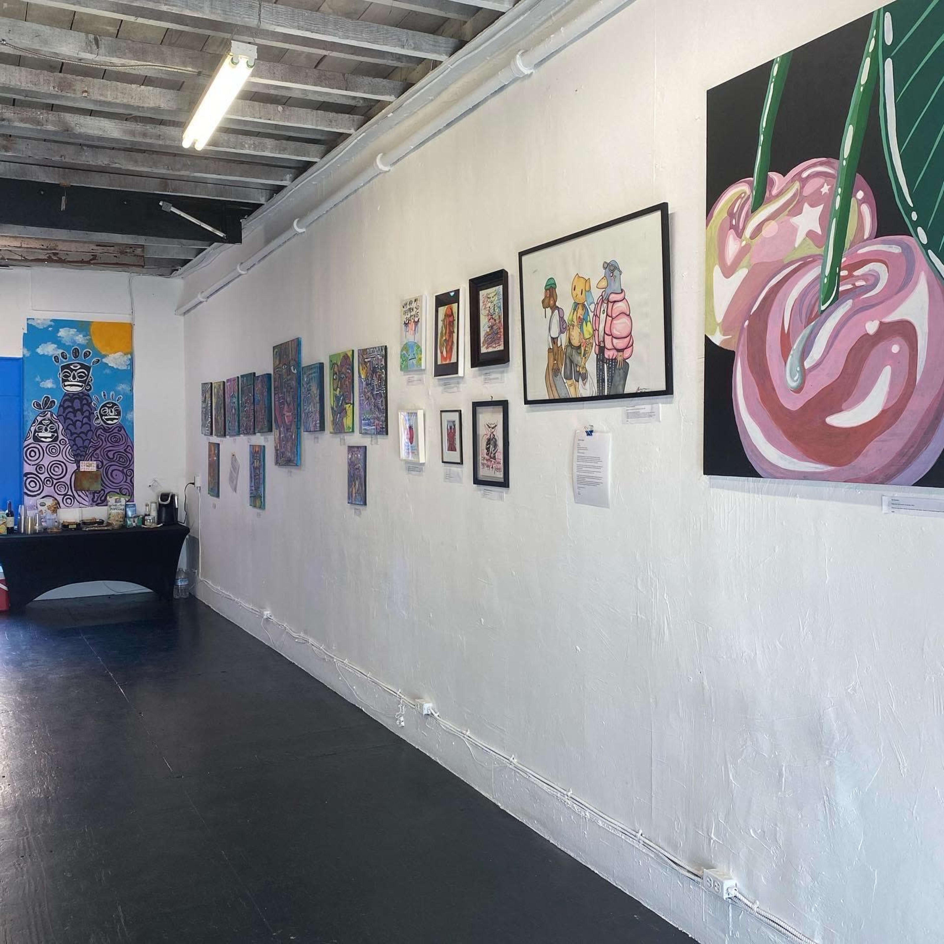 An art gallery featuring various framed artworks displayed on a white wall, with a black table positioned in front.