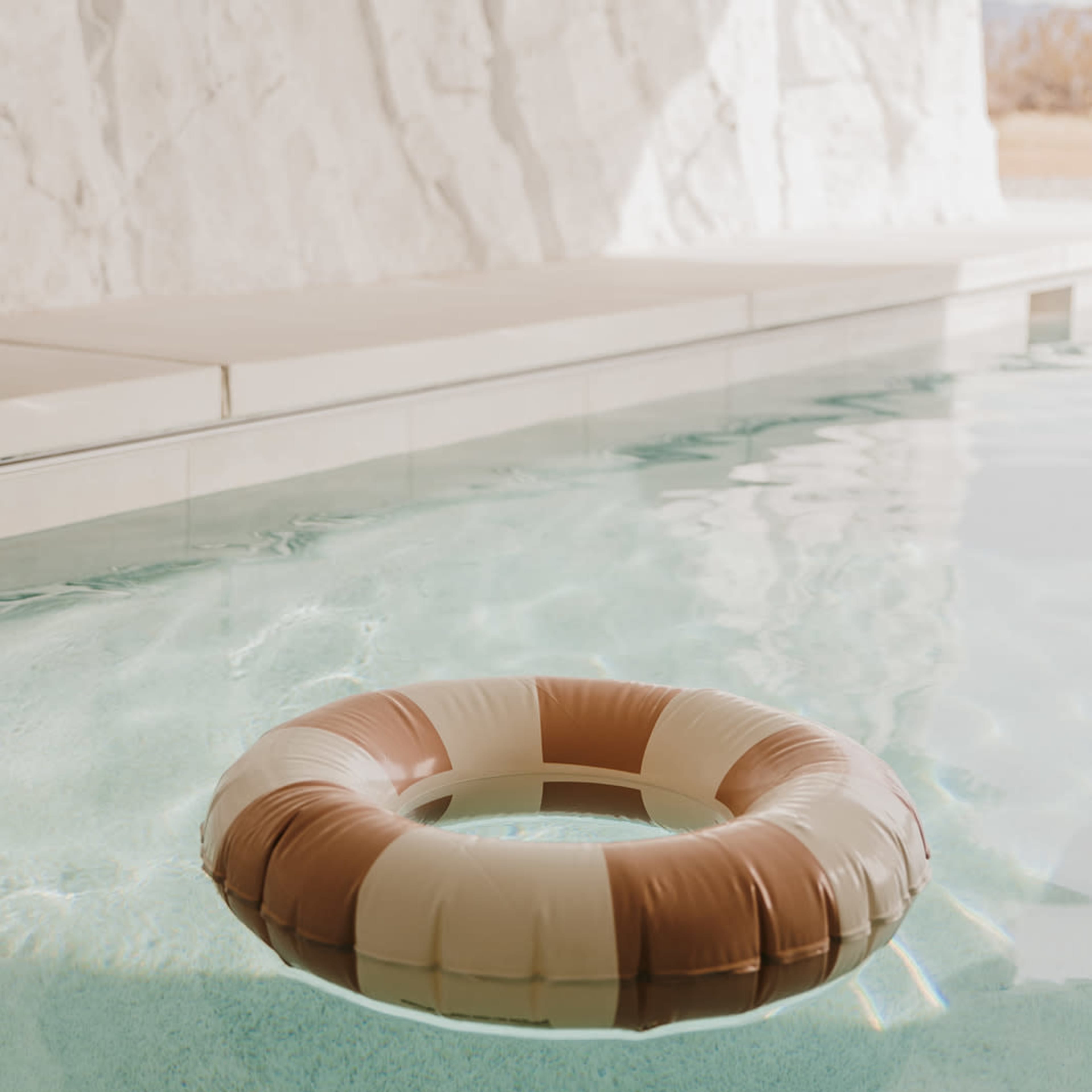 A lifebuoy floats in a clear swimming pool beside a white rock wall.