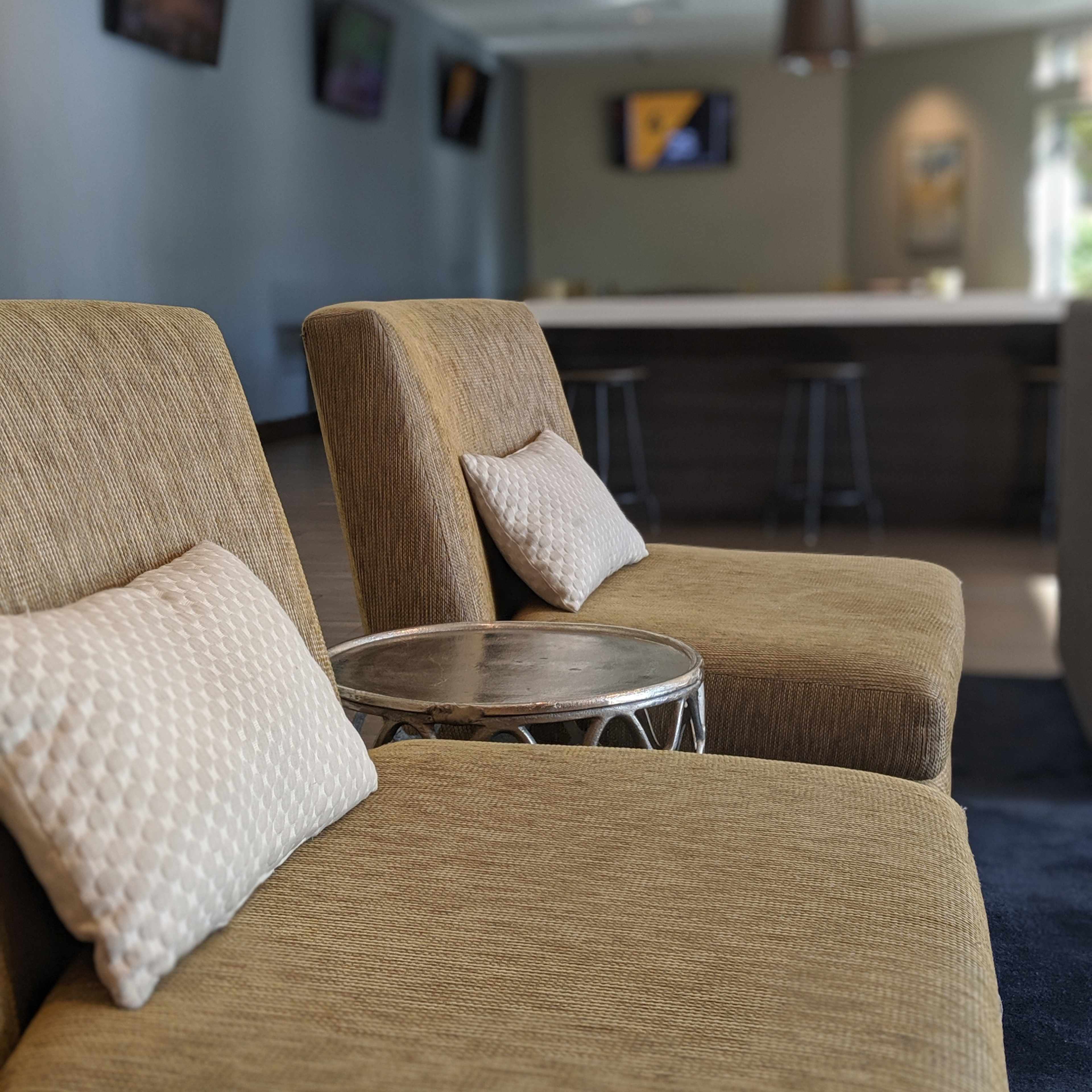 Two modern chairs with cushions beside a small circular table in a lounge area that features a bar in the background.