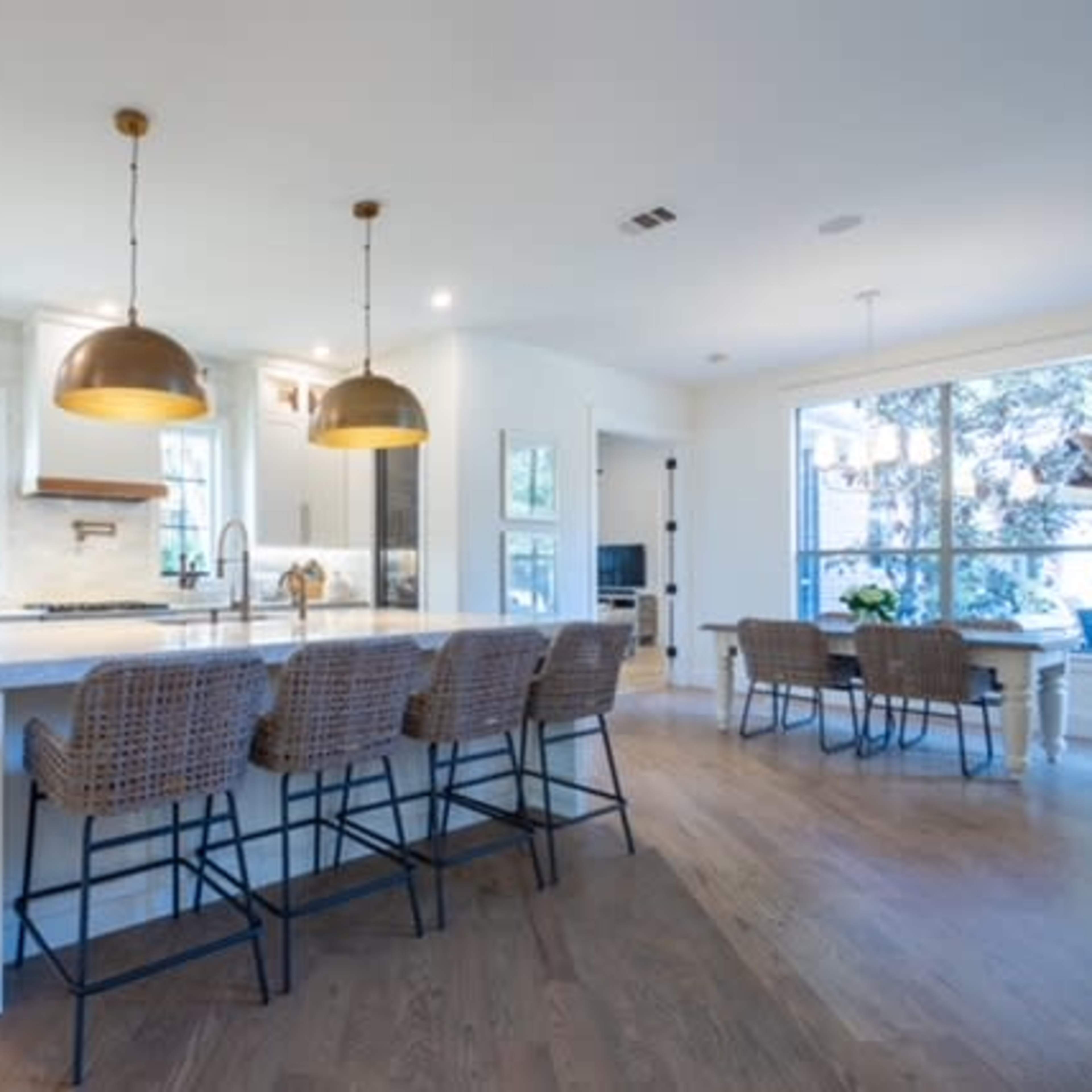 A modern kitchen with white cabinetry, a large island with bar stools, and pendant lighting, adjacent to a dining area with large windows.