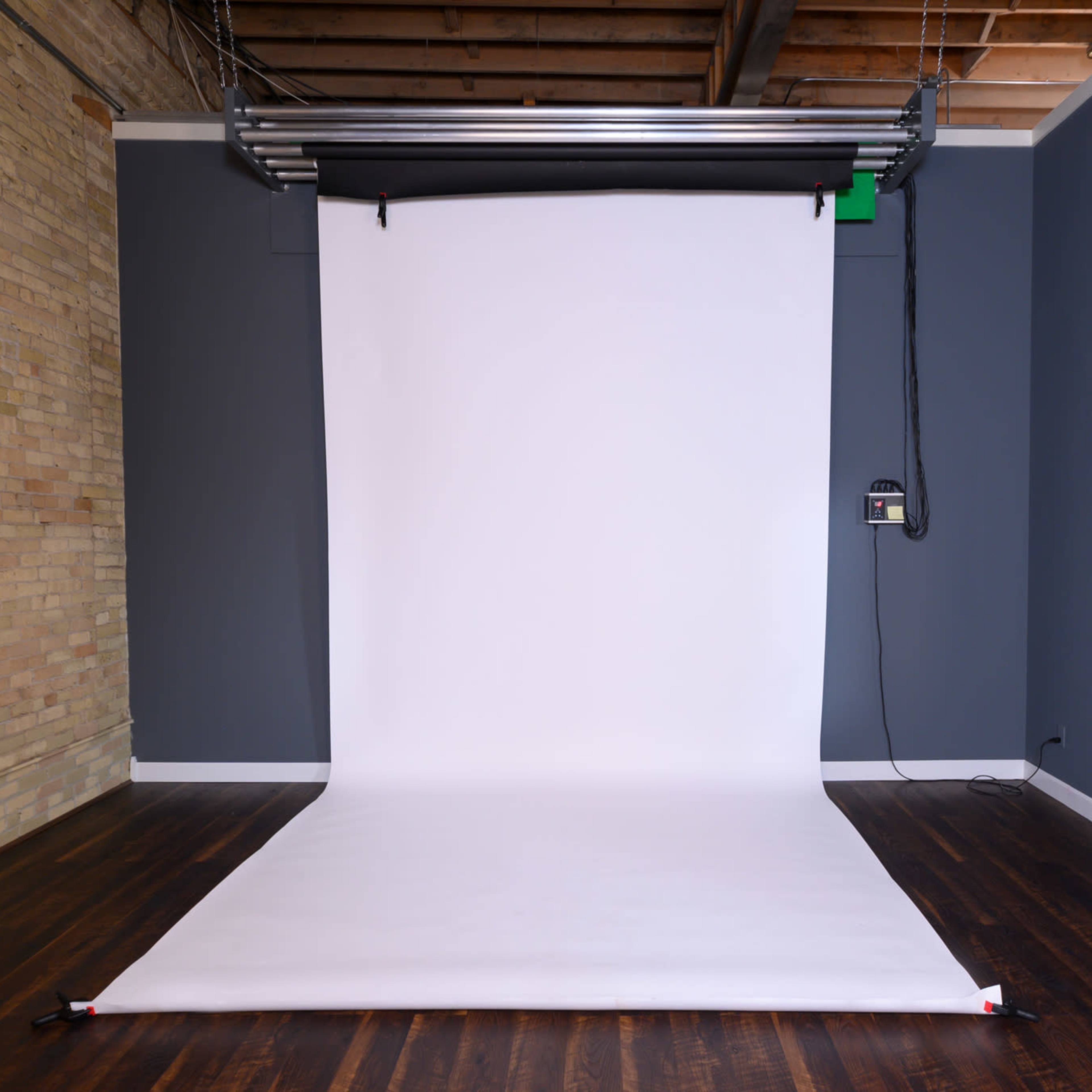A photography studio with a clean white backdrop set up against a gray wall and a mirror on the right.