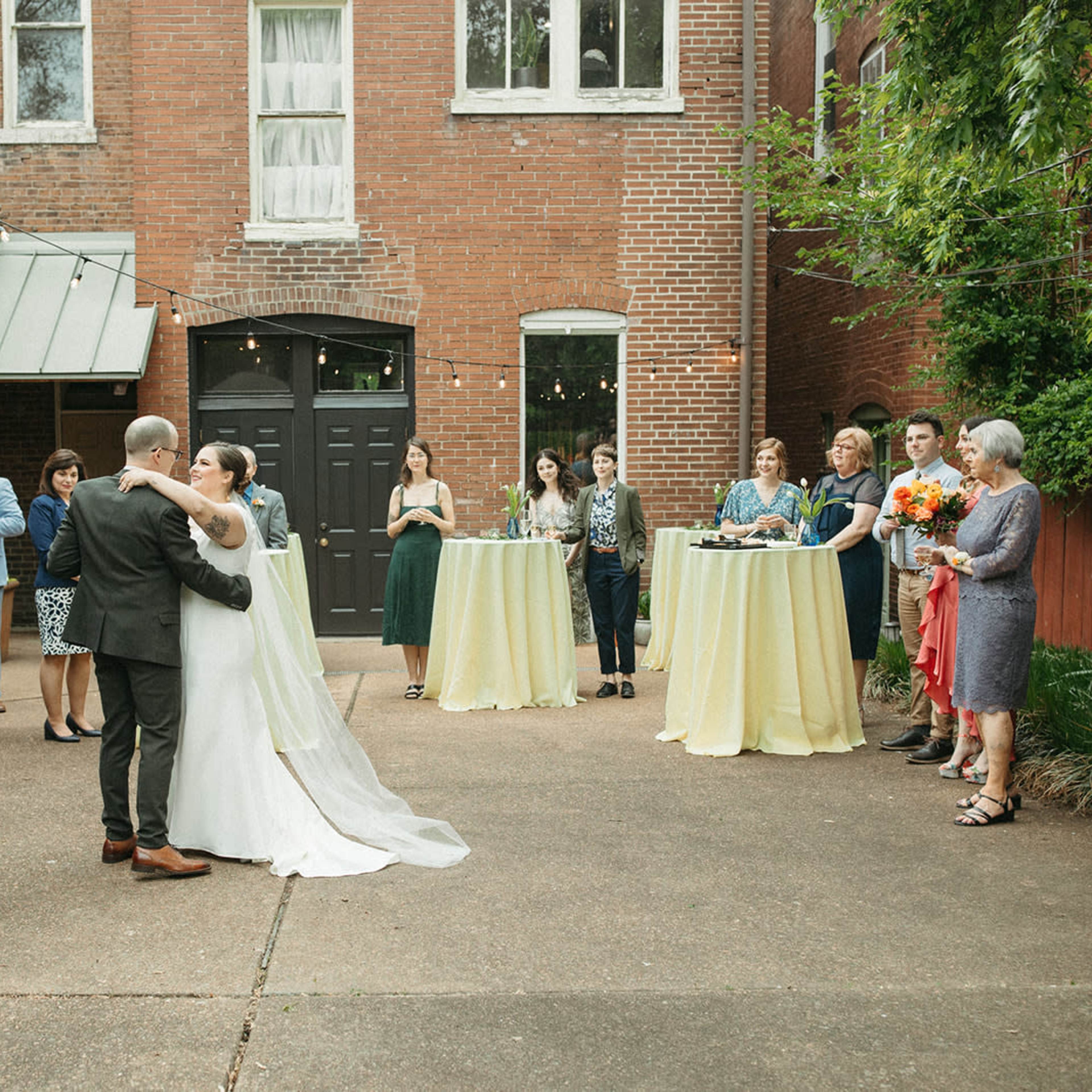 A couple dances together in an outdoor courtyard surrounded by guests during a wedding celebration.