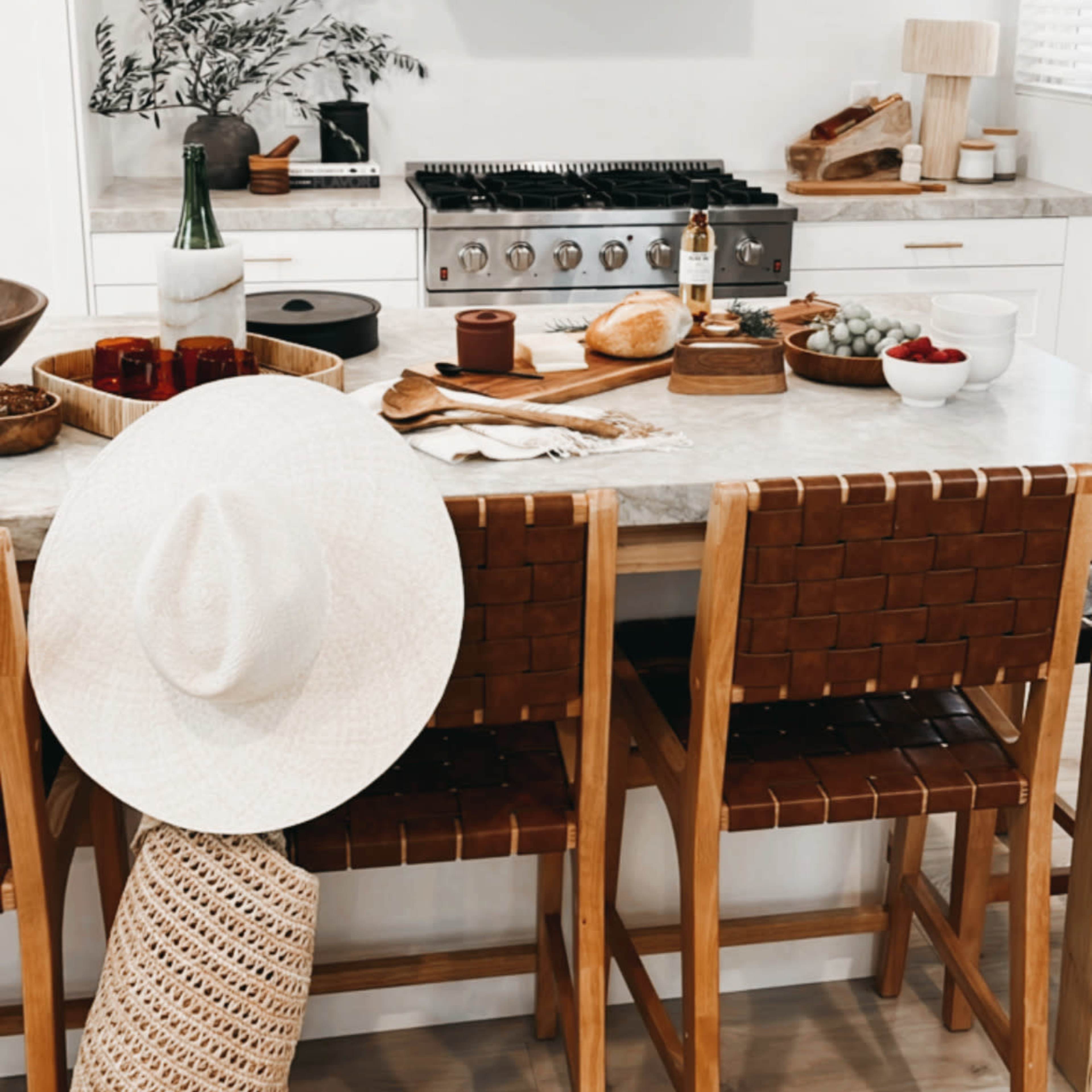 The kitchen features a modern design with a large gas stove, wooden bar stools, and a table set with various food items and decorative elements.