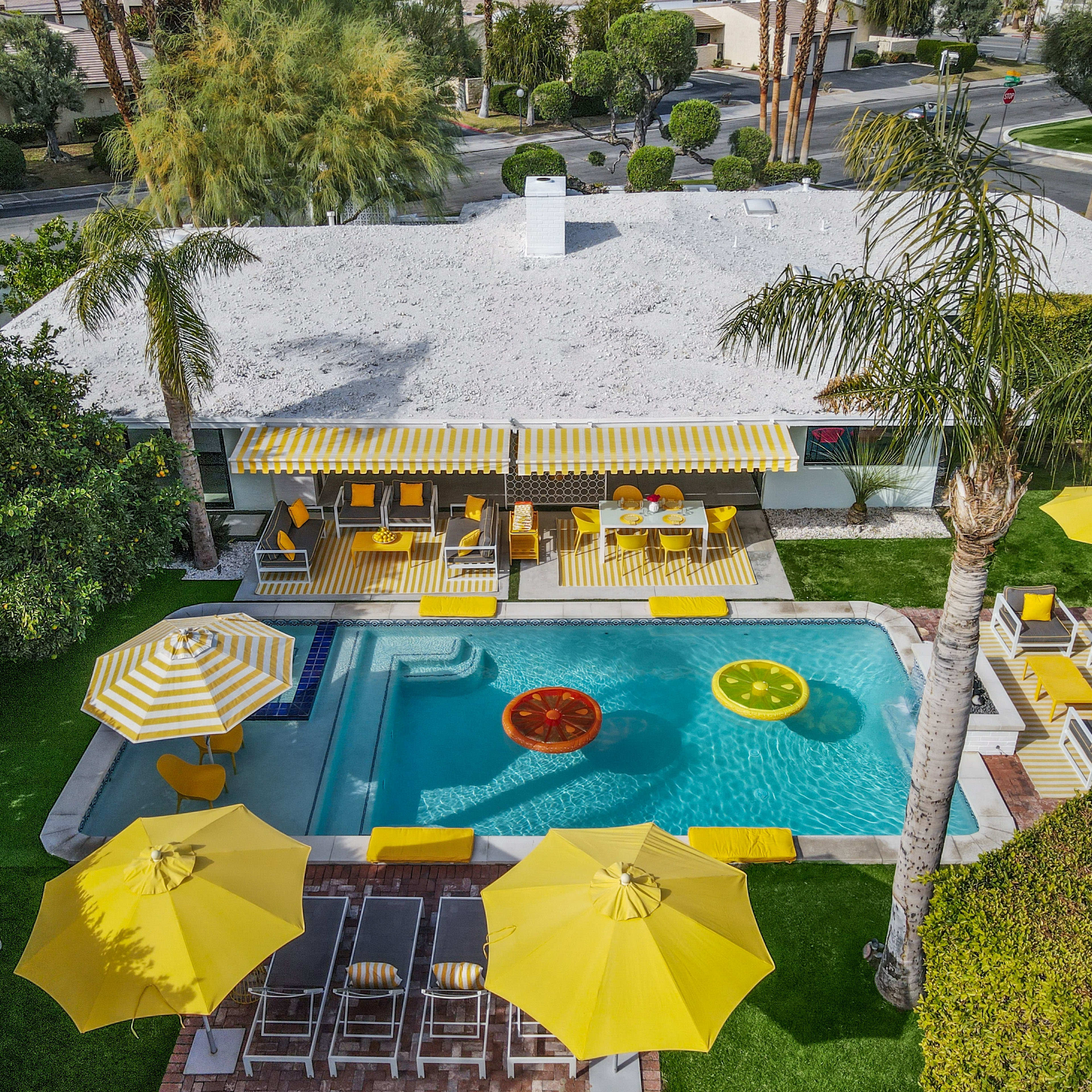 A backyard pool area with a modern house, featuring yellow umbrellas and lounge chairs around a swimming pool.