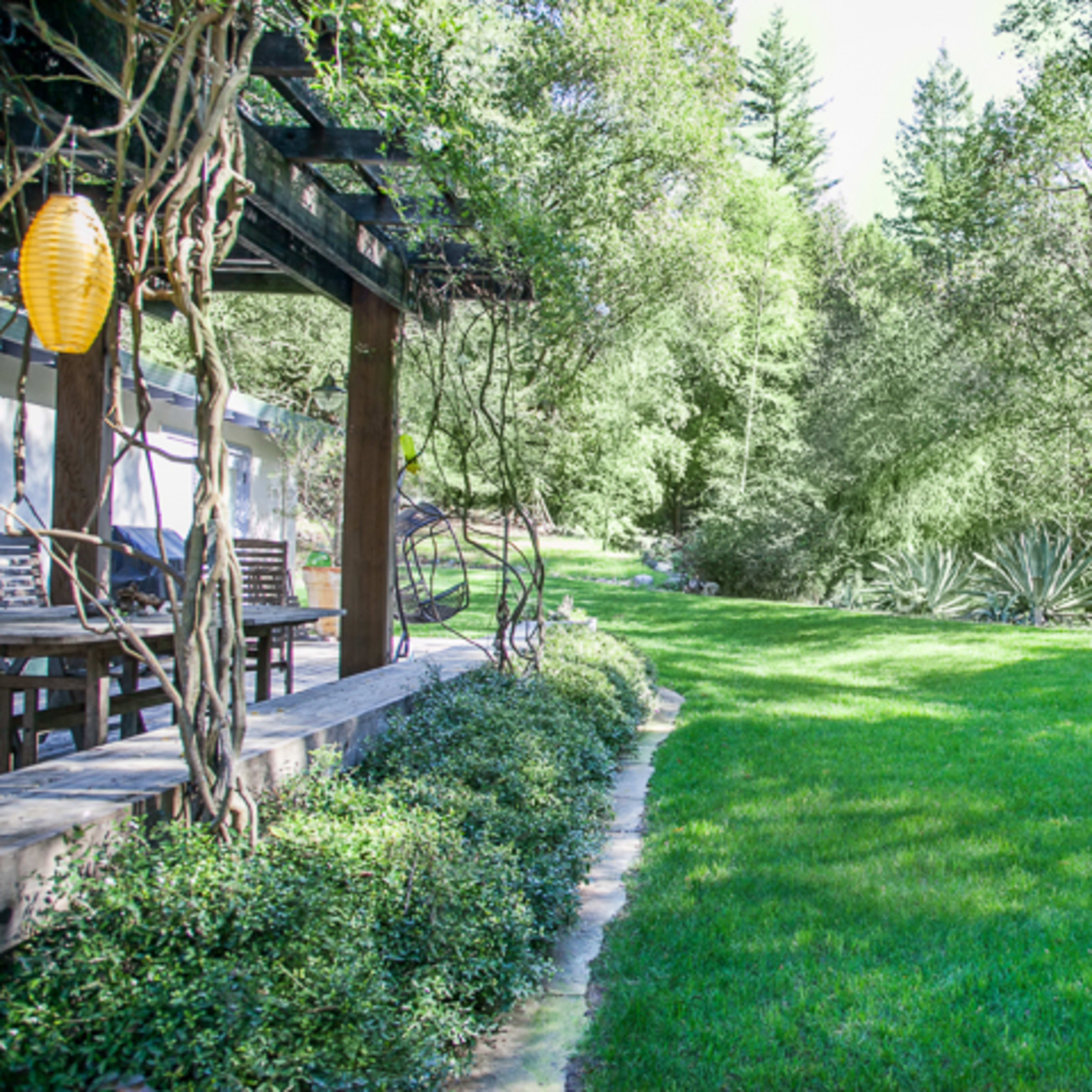 A well-manicured lawn surrounded by trees and shrubs, with a patio area featuring outdoor furniture to the side.