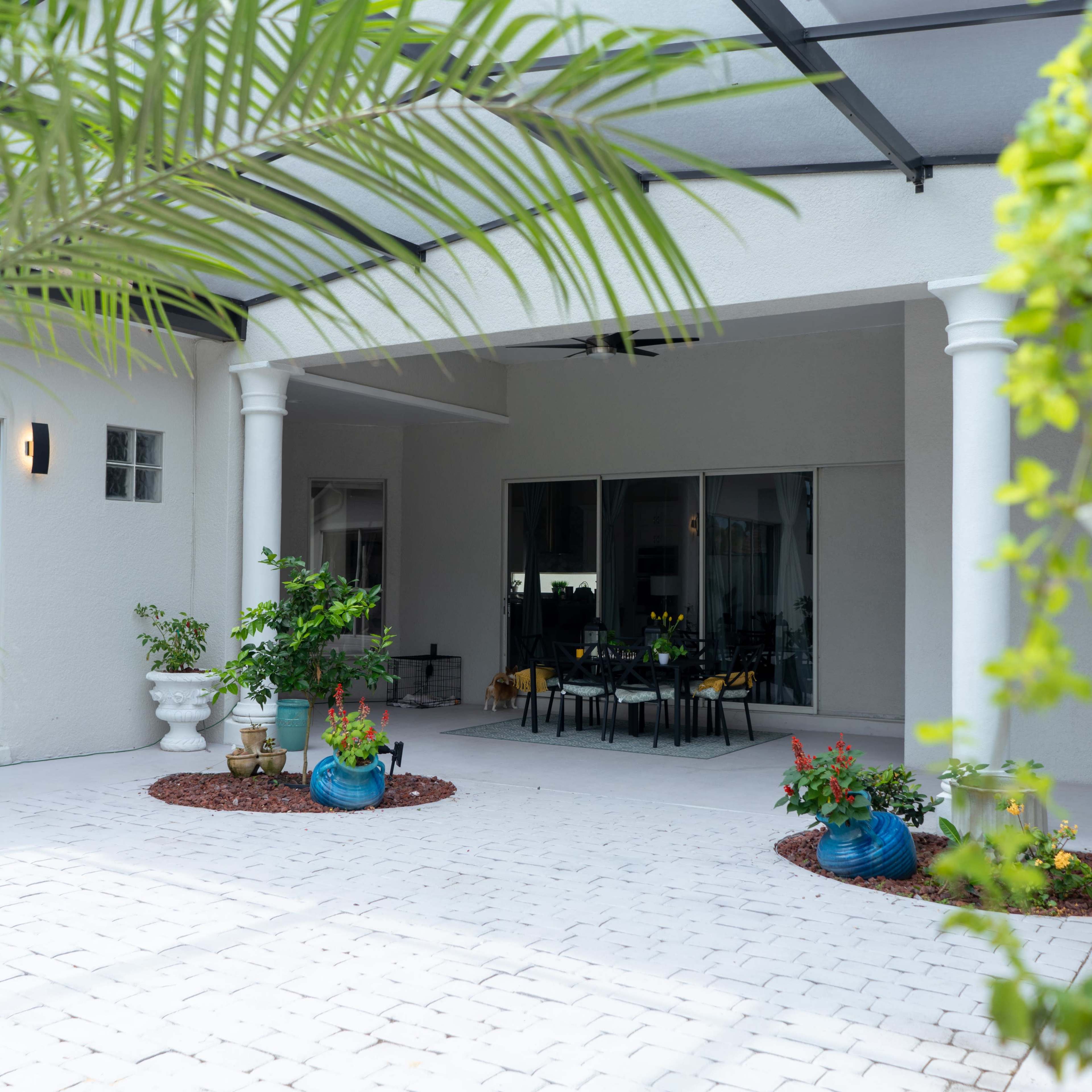 A patio area with potted plants, a table and chairs under a covered structure, and a smooth stone floor.
