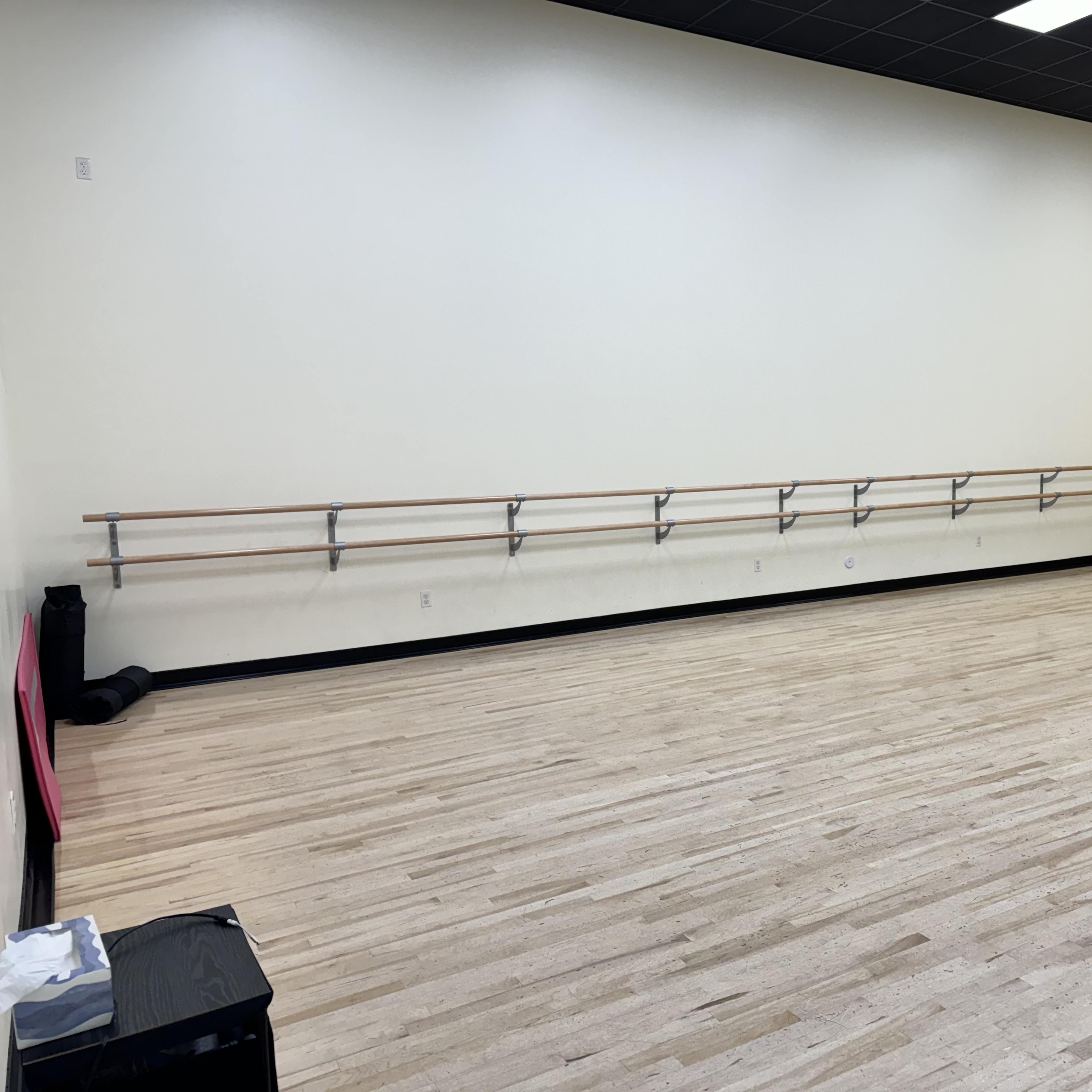 A spacious dance studio with polished wooden floors and ballet barres mounted on the wall.