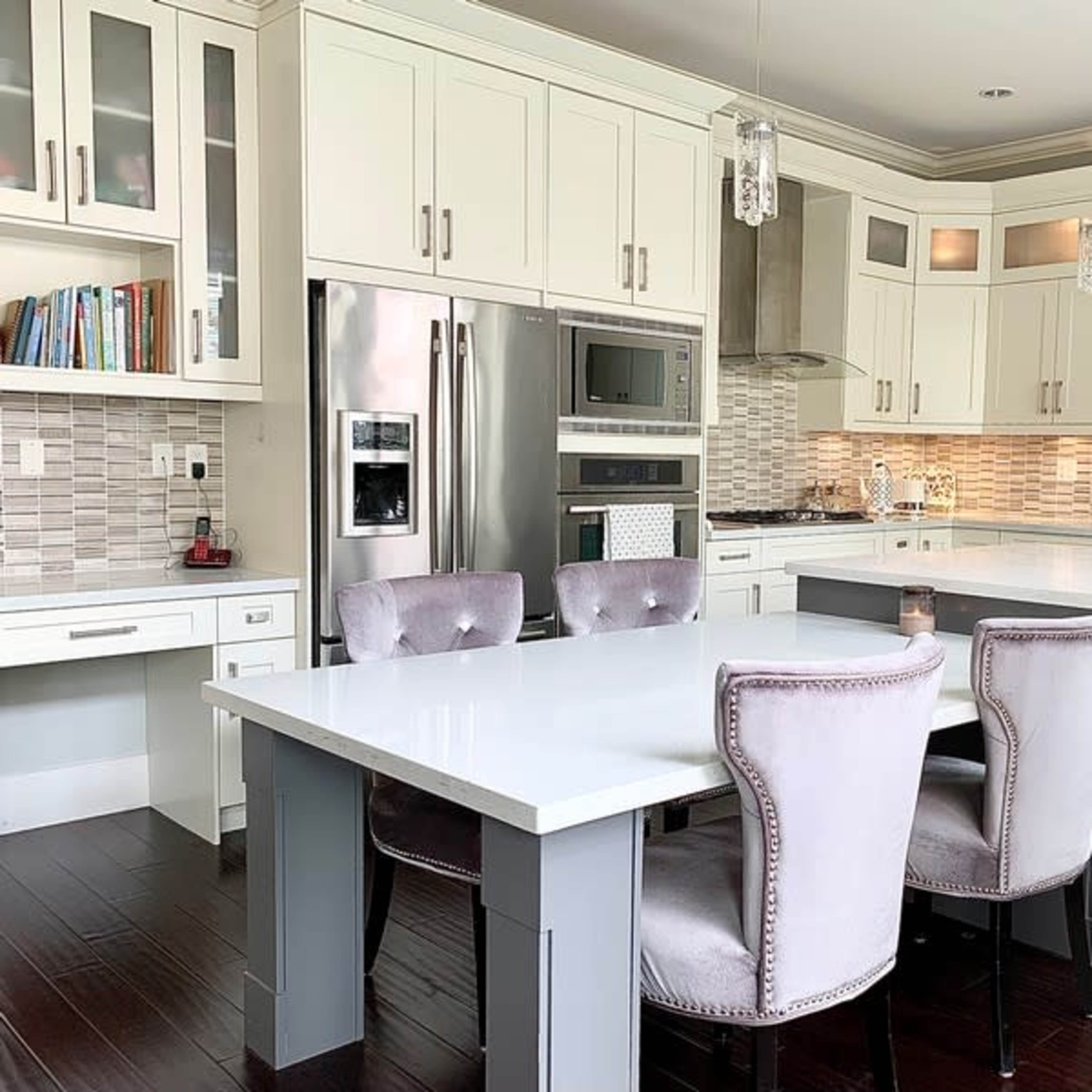 A modern kitchen featuring white cabinetry, stainless steel appliances, and a central island with gray accents and upholstered chairs.