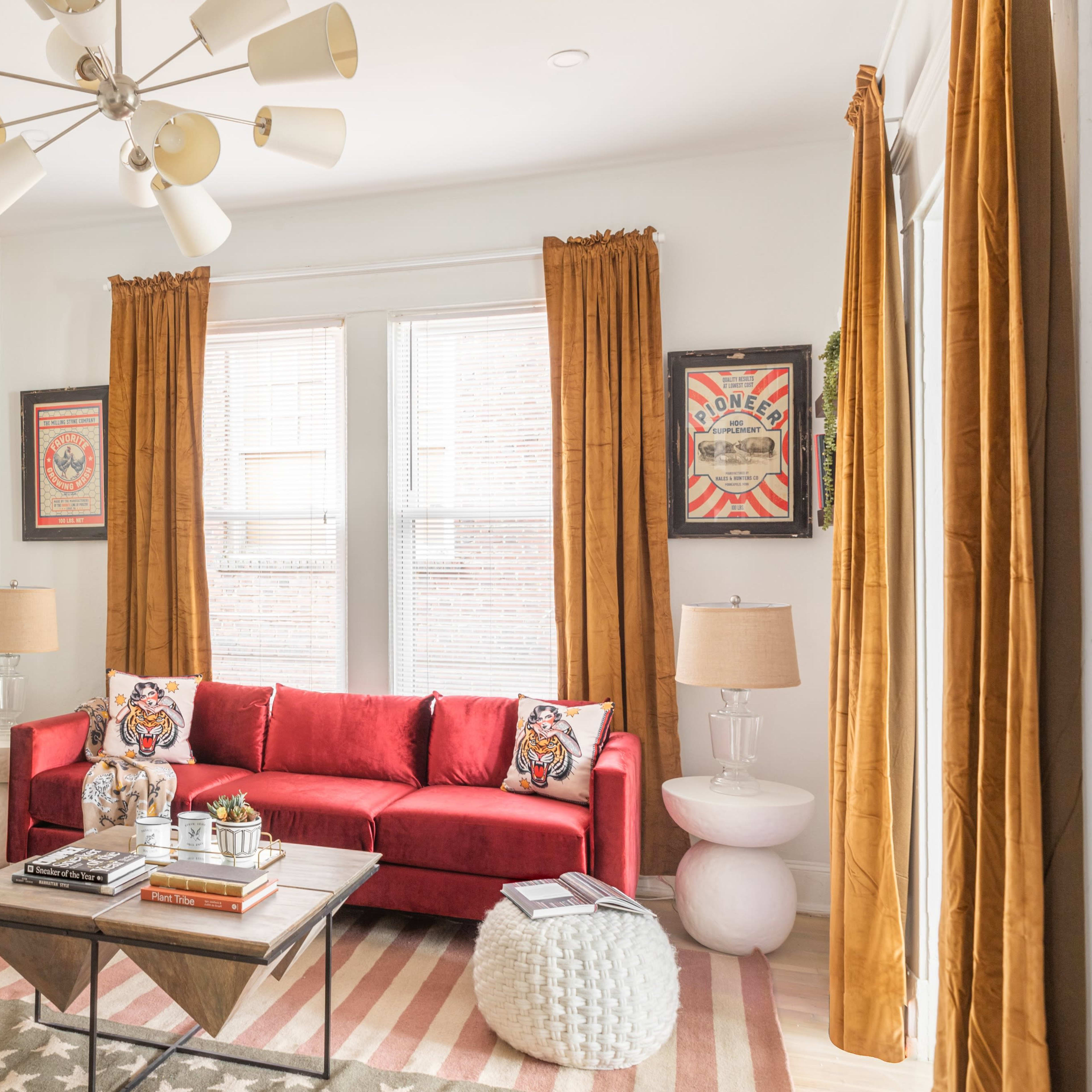 The living room features a red sofa, a patterned area rug, and large windows with yellow curtains, complemented by decorative wall art and modern lighting.