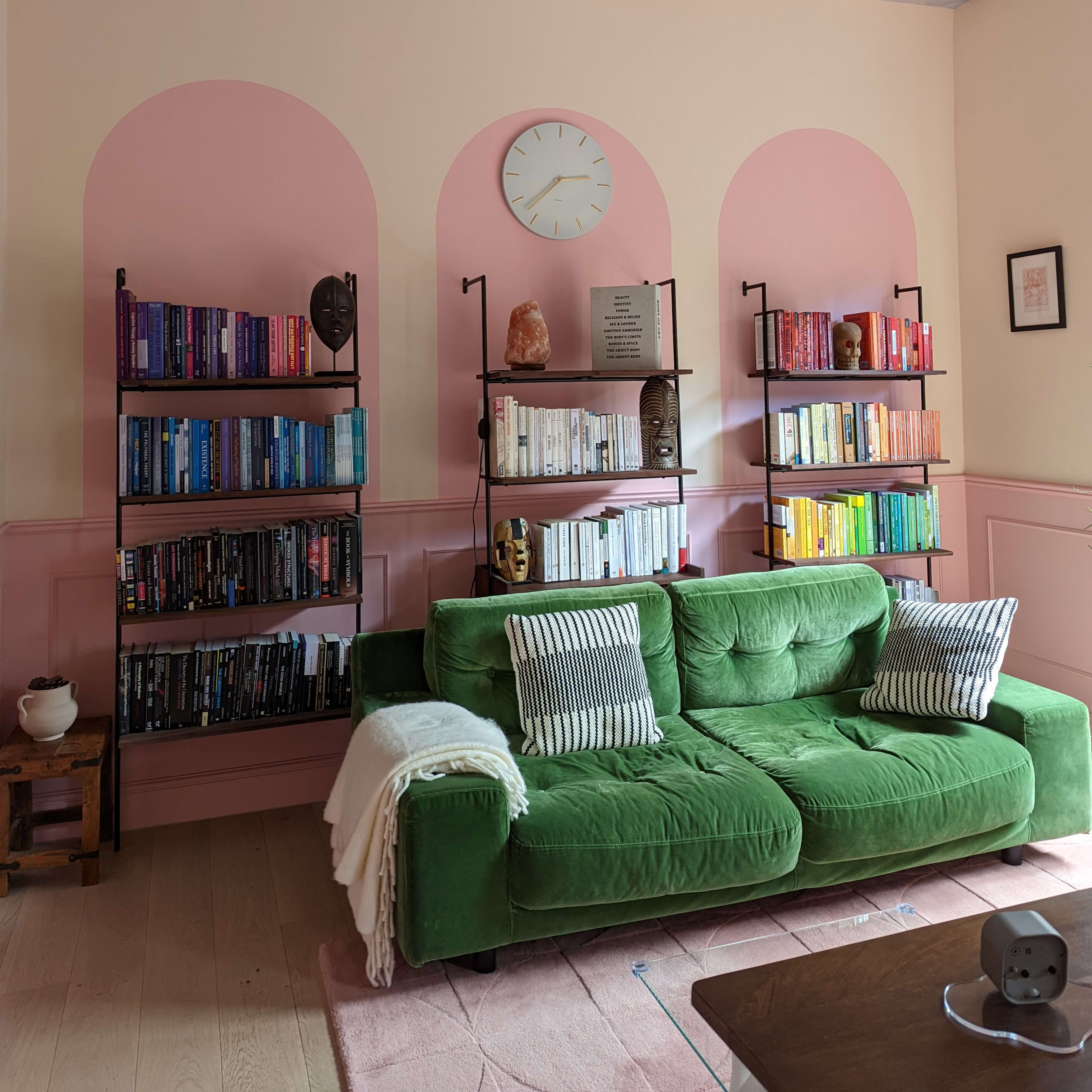A cozy reading nook with a green couch, two bookshelf units filled with colorful books, and a ceiling painted with clouds.