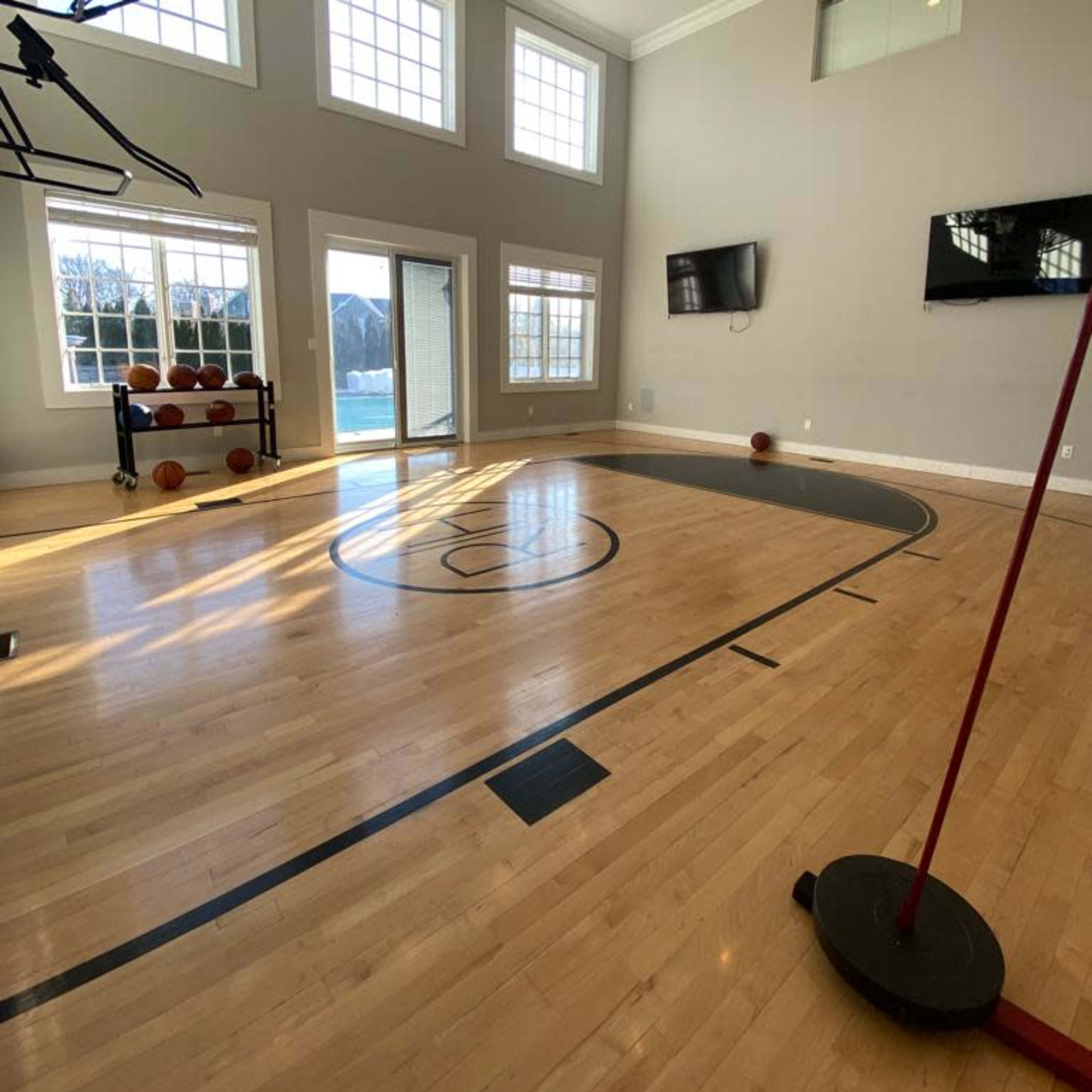 An indoor basketball court with a hoop, hardwood flooring, and large windows that provide natural light.