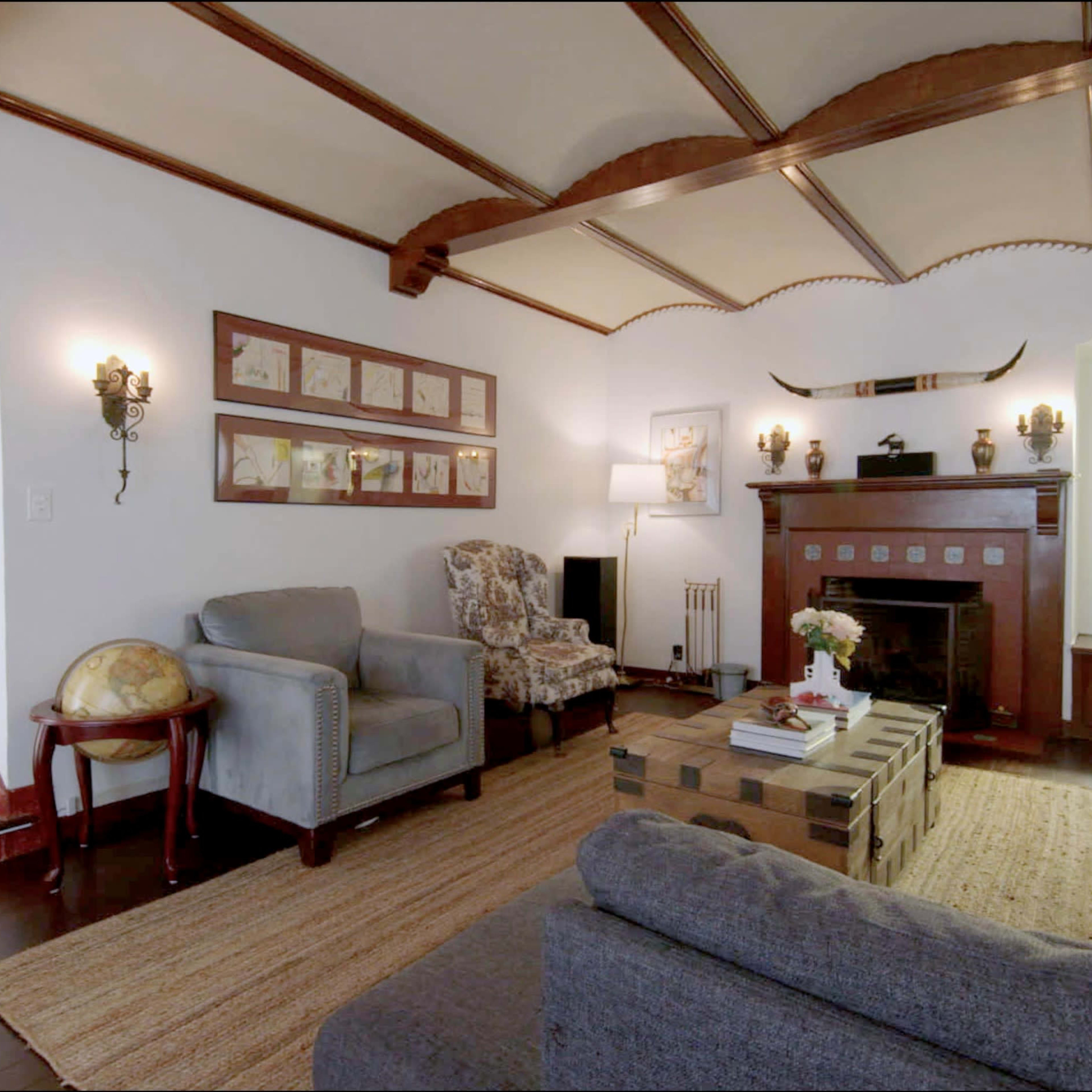 A cozy living room features two sofas, an armchair, a coffee table on a textured rug, and a fireplace adorned with decorative elements.