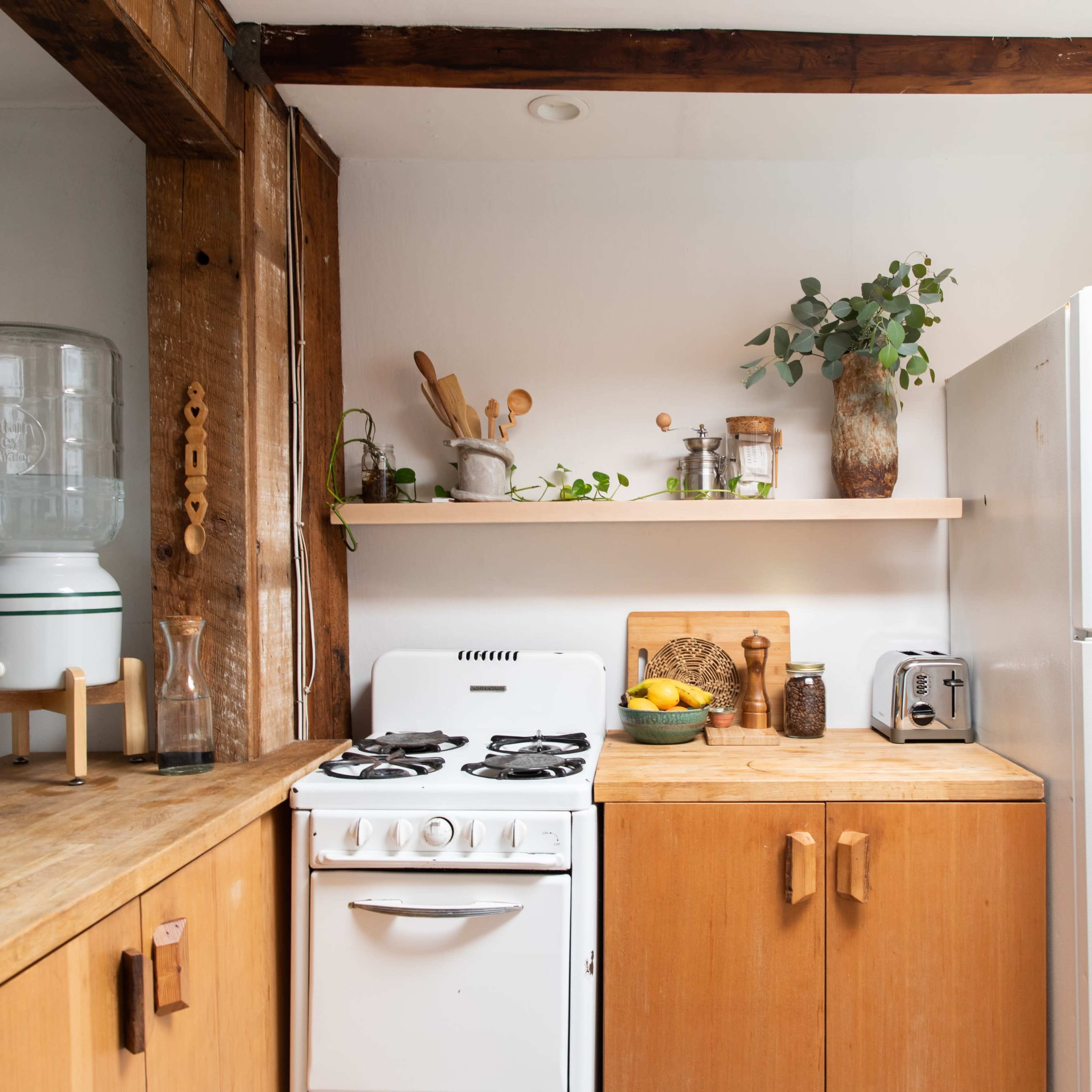 A small kitchen with wooden cabinetry, a white refrigerator, a stove, and various kitchen utensils on a shelf.