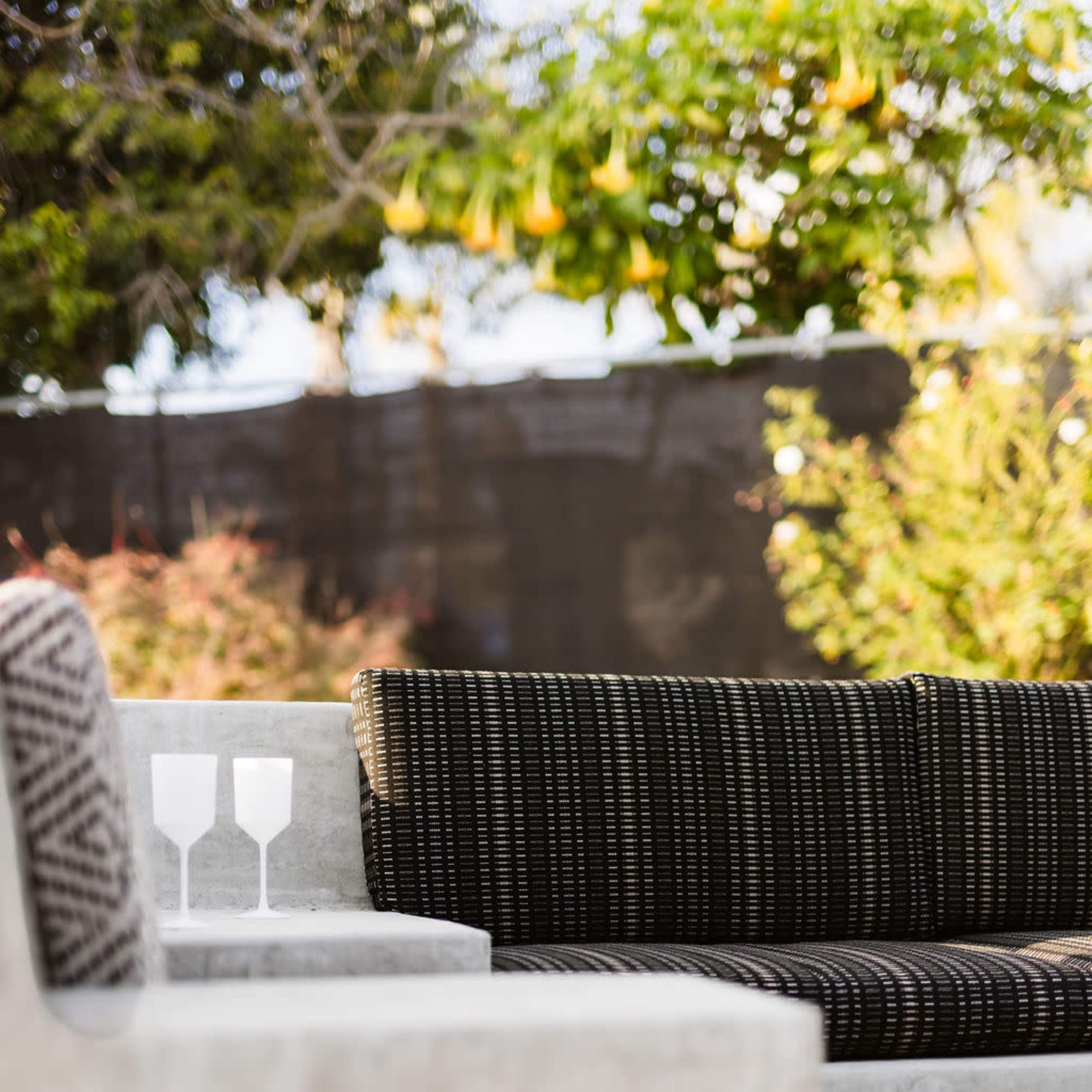 A modern outdoor seating area featuring a black woven couch and three glasses placed on a light-colored table.