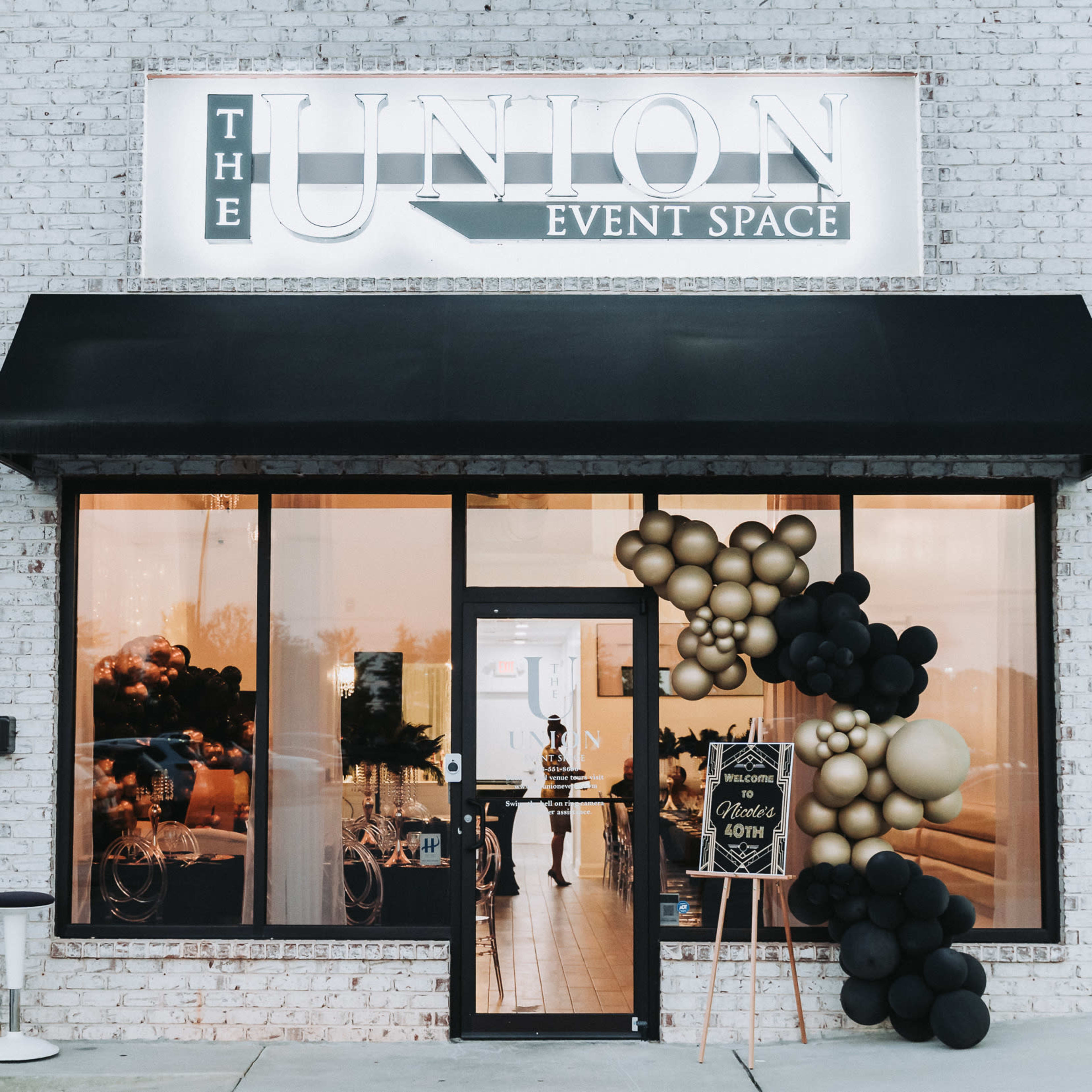 The entrance of "The Union Event Space," featuring a decorative sign, large windows, and a balloon arch in black and gold.
