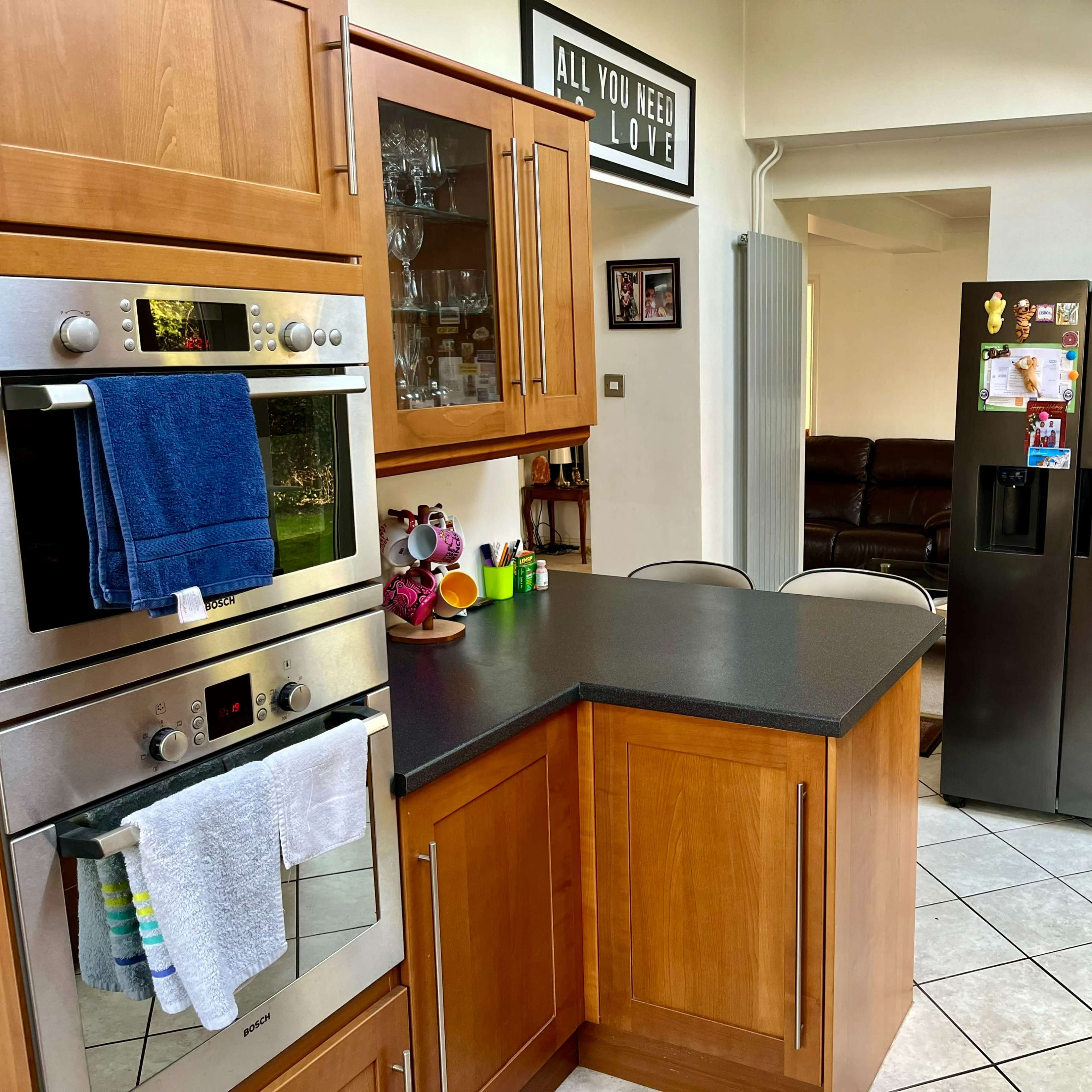 The kitchen features wooden cabinets, a stainless steel oven, and a black refrigerator adorned with various magnets and notes.