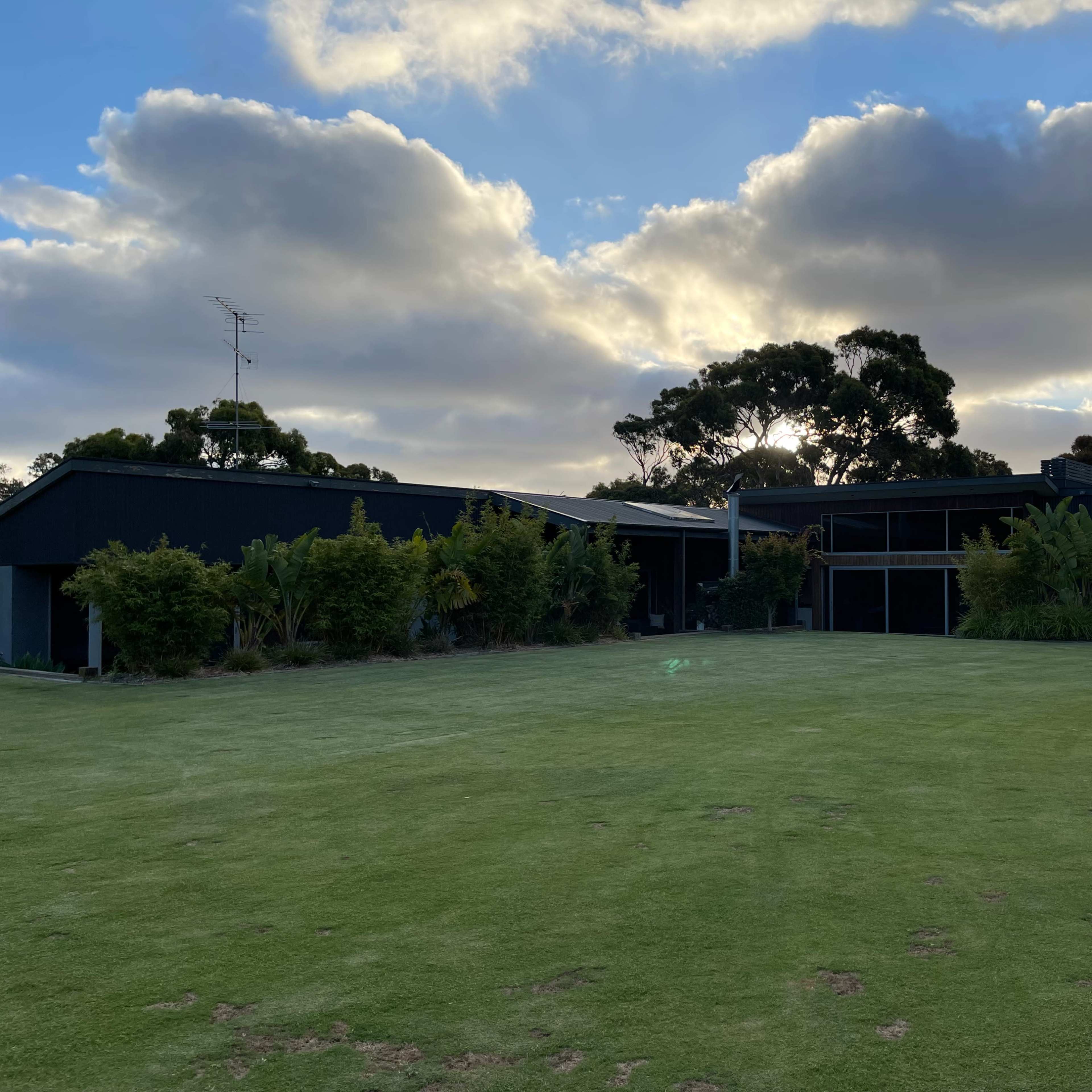 A modern black house is set against a cloudy sky, with a lush green lawn and surrounding landscaping.