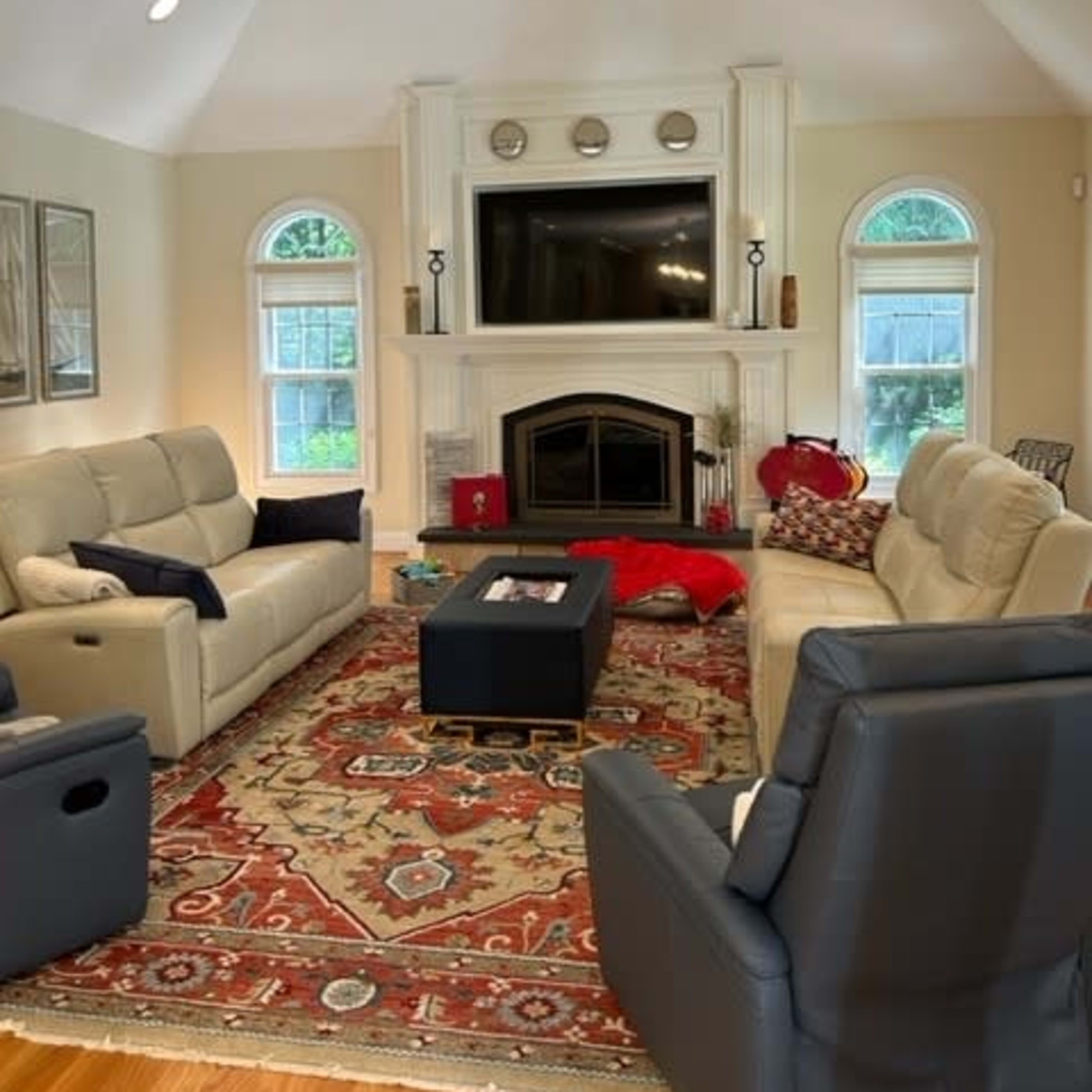 The living room features two sofas facing a central coffee table, with a large fireplace and a television mounted above a mantel.
