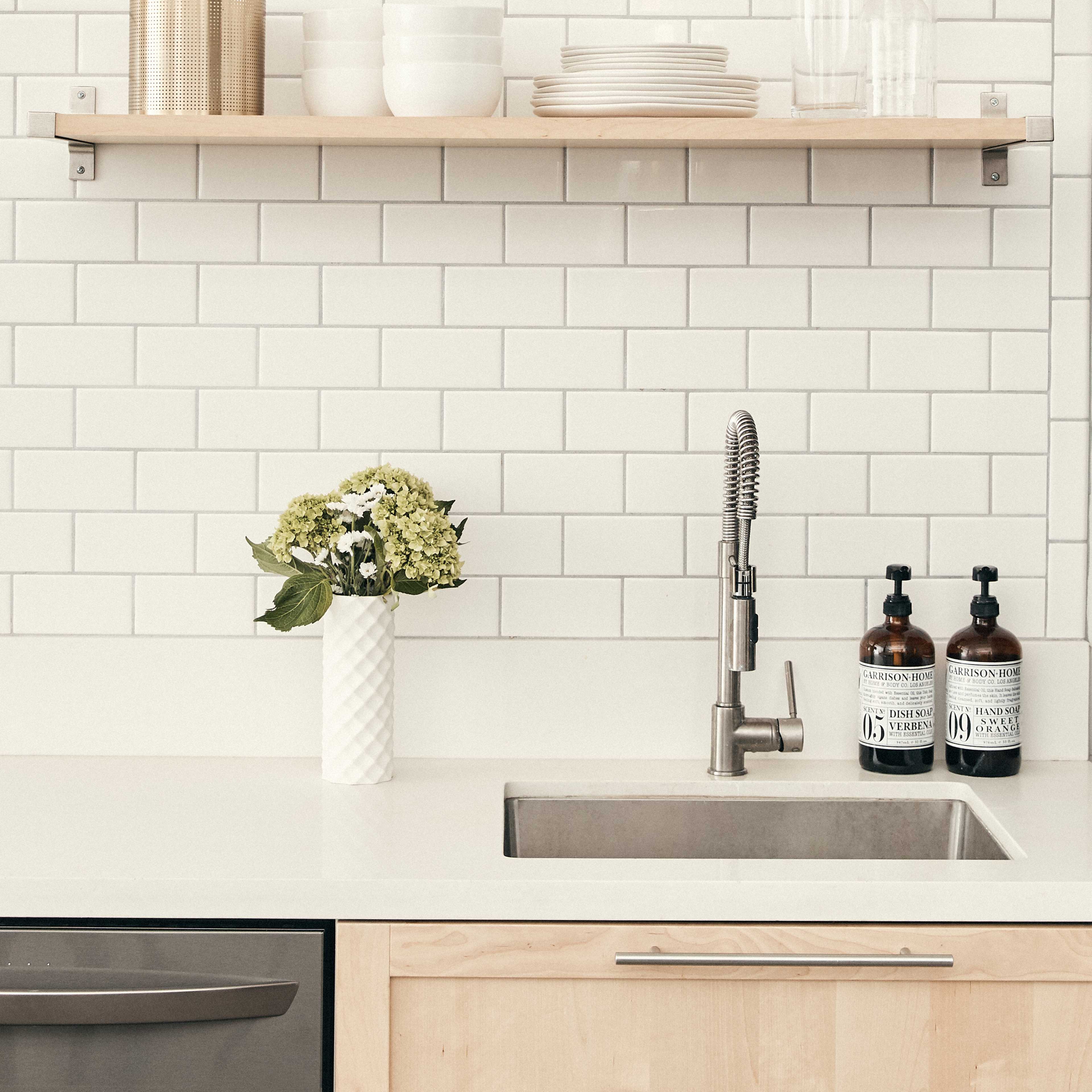 A minimalist kitchen countertop with a sink, a wooden shelf holding dishware, and a vase of flowers.