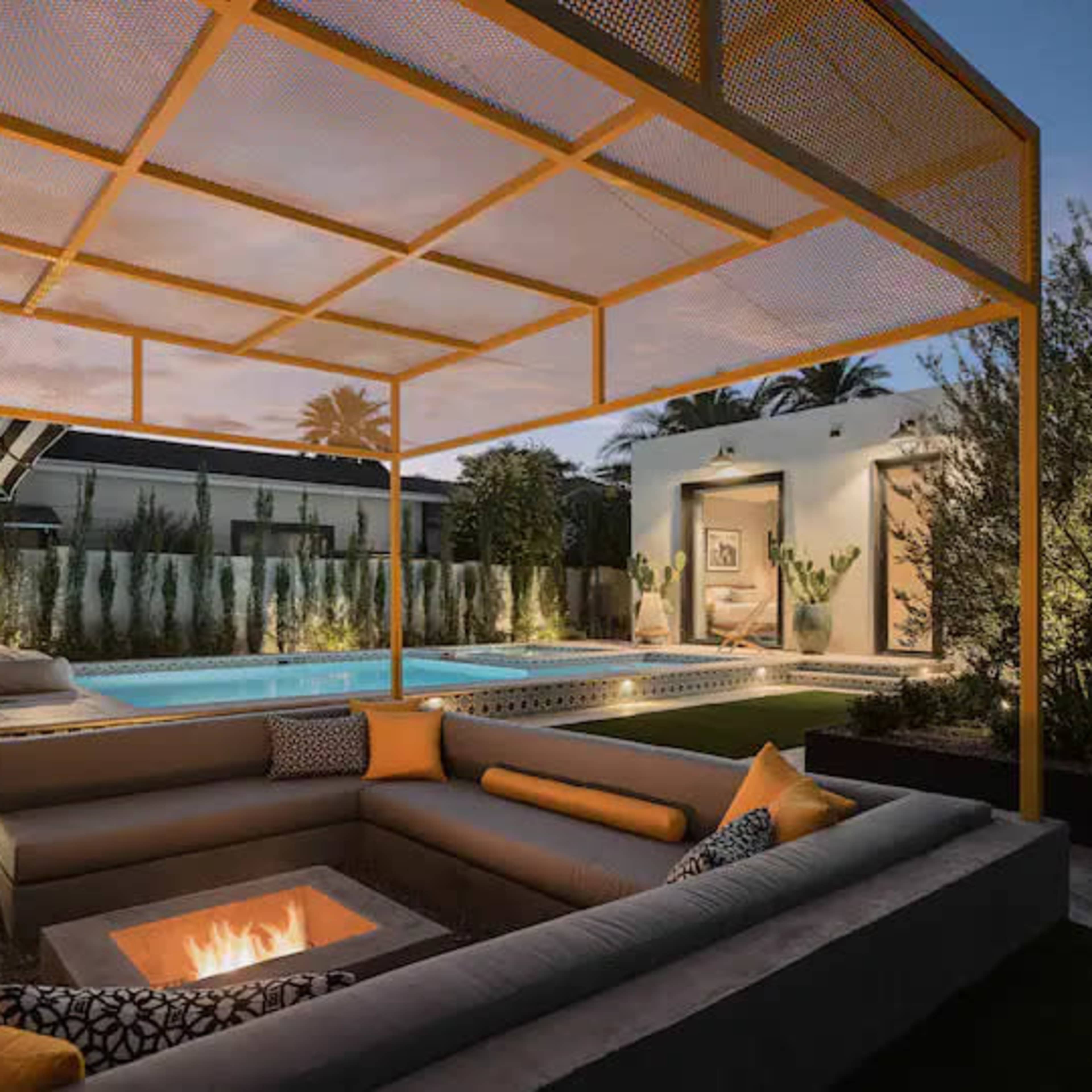 A modern outdoor seating area features a fire pit and a shaded pergola overlooking a swimming pool amidst landscaped greenery.