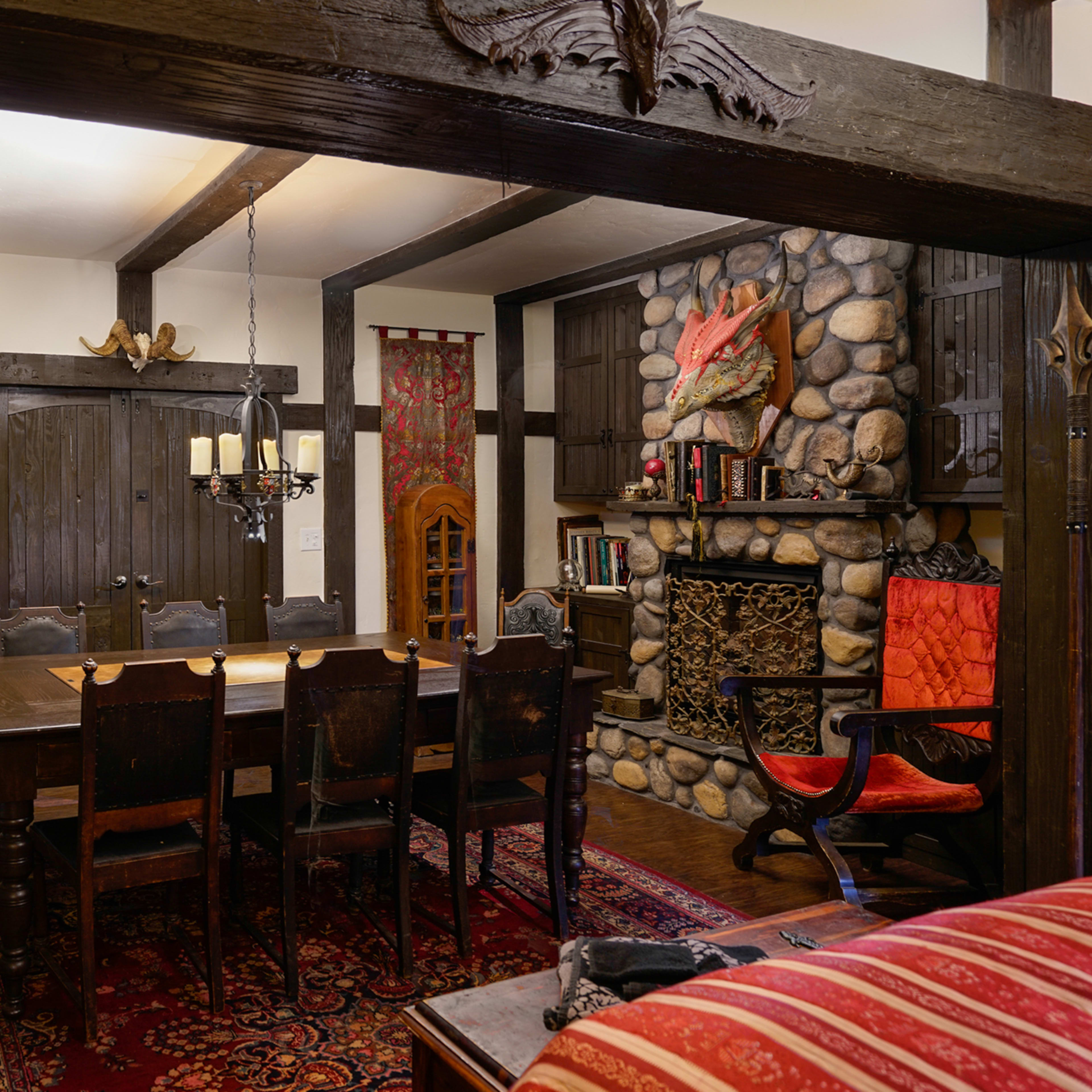 A rustic dining room featuring a large wooden table surrounded by chairs, a stone fireplace, and decorative banners on the walls.