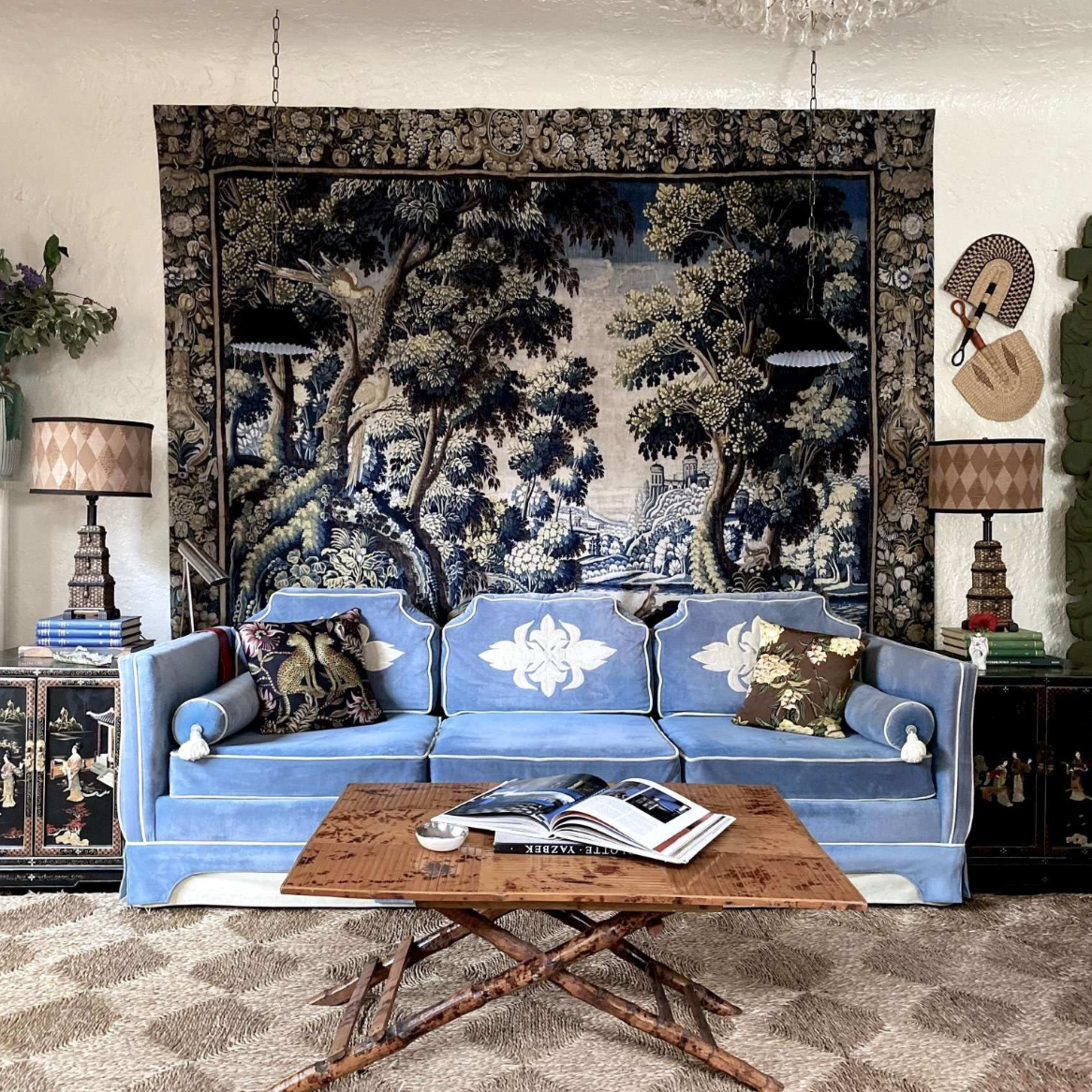 A living room with a blue upholstered sofa, a wooden coffee table, and a decorative tapestry hanging on the wall behind the sofa.