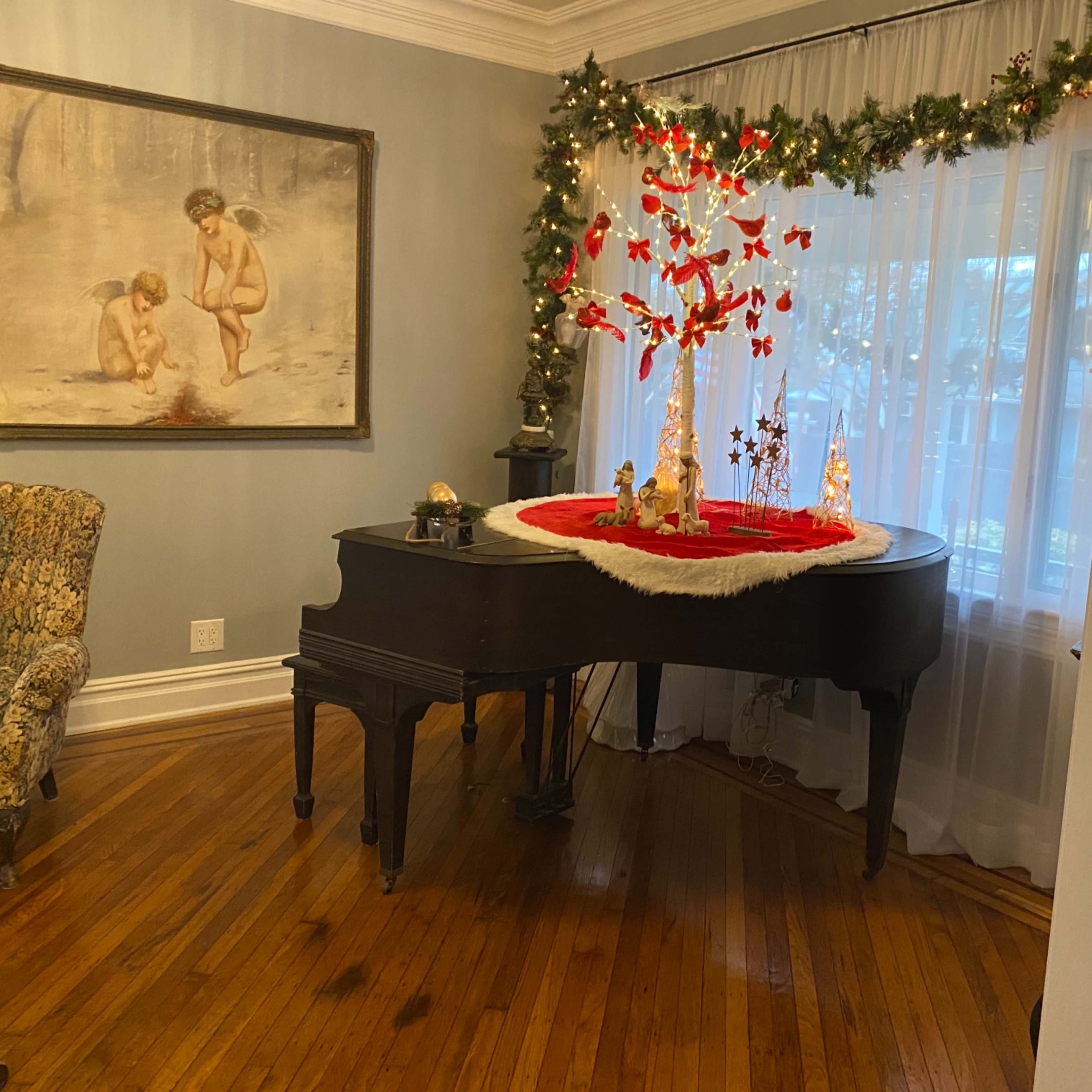 A grand piano is centered in a room decorated with a red and white holiday setting, surrounded by a floral-patterned armchair and a large painting on the wall.