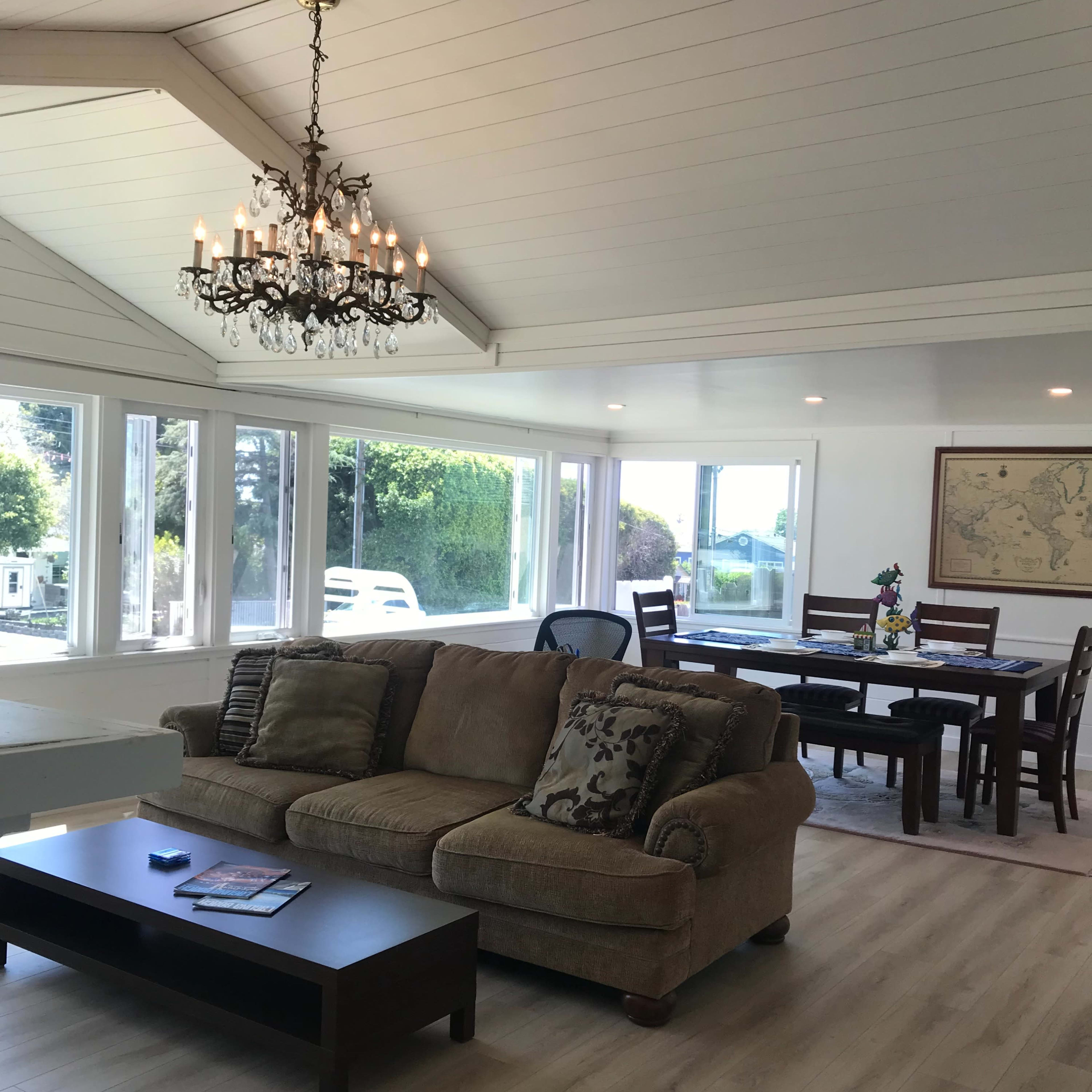 A bright living space featuring a sofa, a chandelier, and a dining area with a table and chairs.