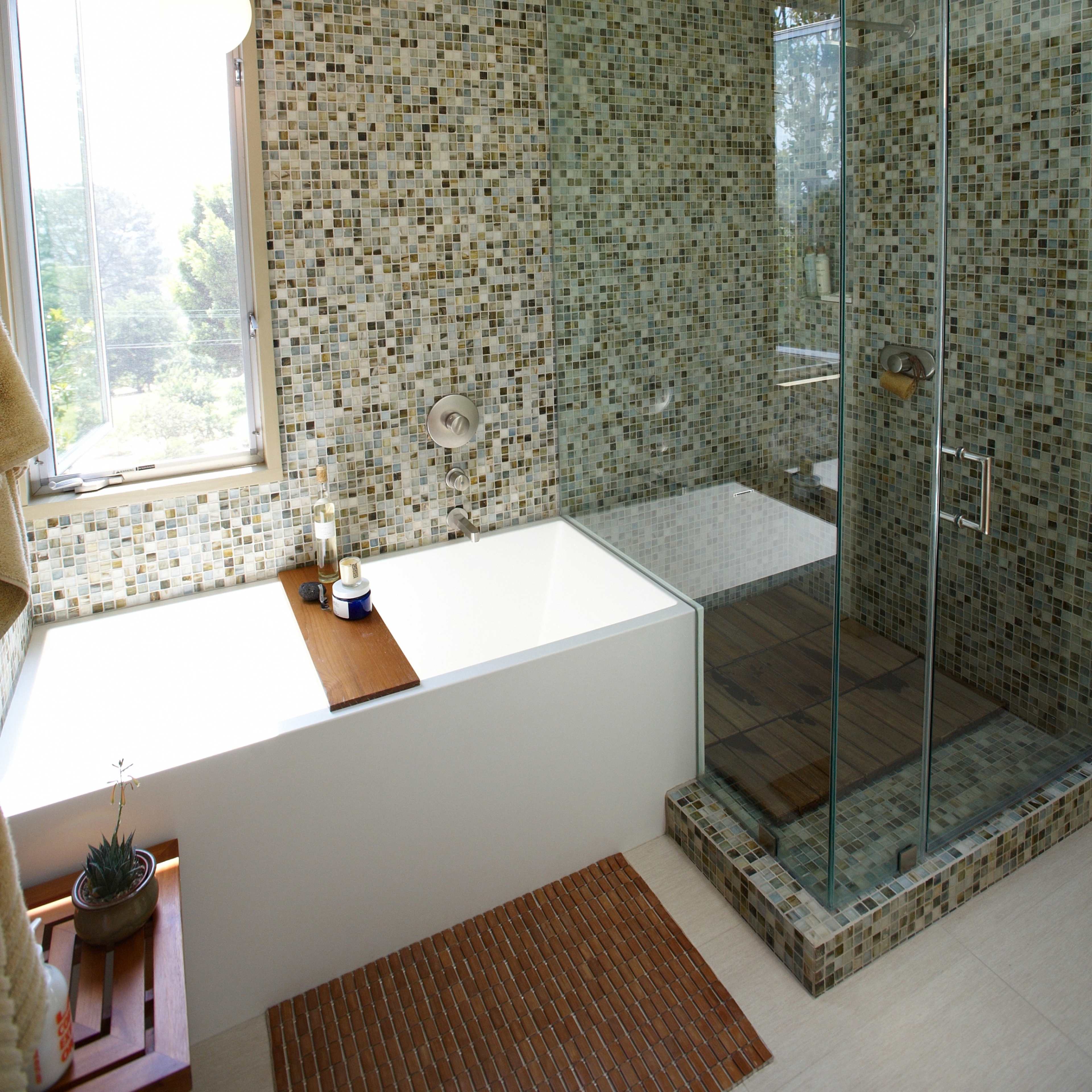 A modern bathroom with a glass shower enclosure, a bathtub, and mosaic tiled walls.