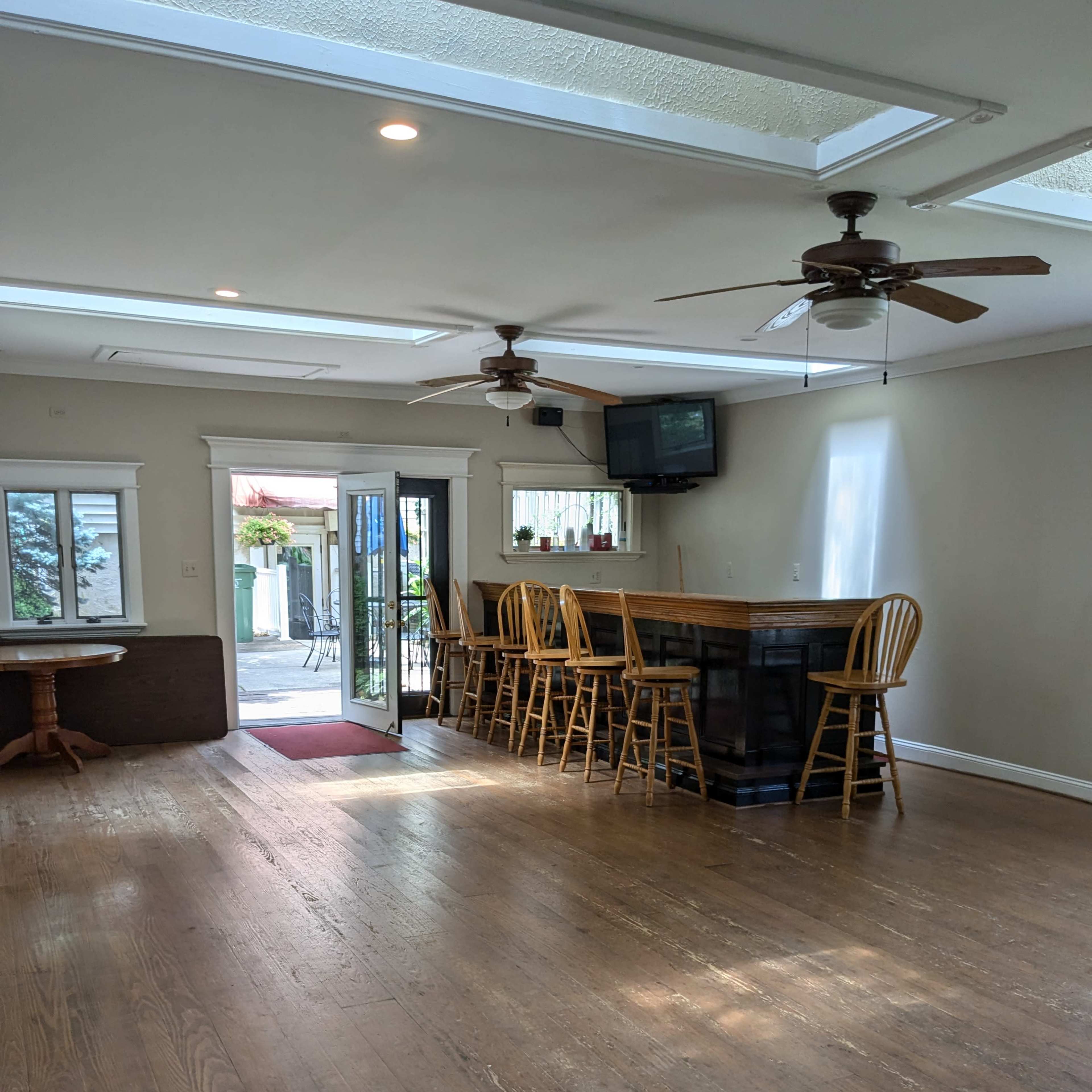 A spacious, well-lit indoor area featuring a bar counter with seating, two ceiling fans, and a door leading to an outdoor space.