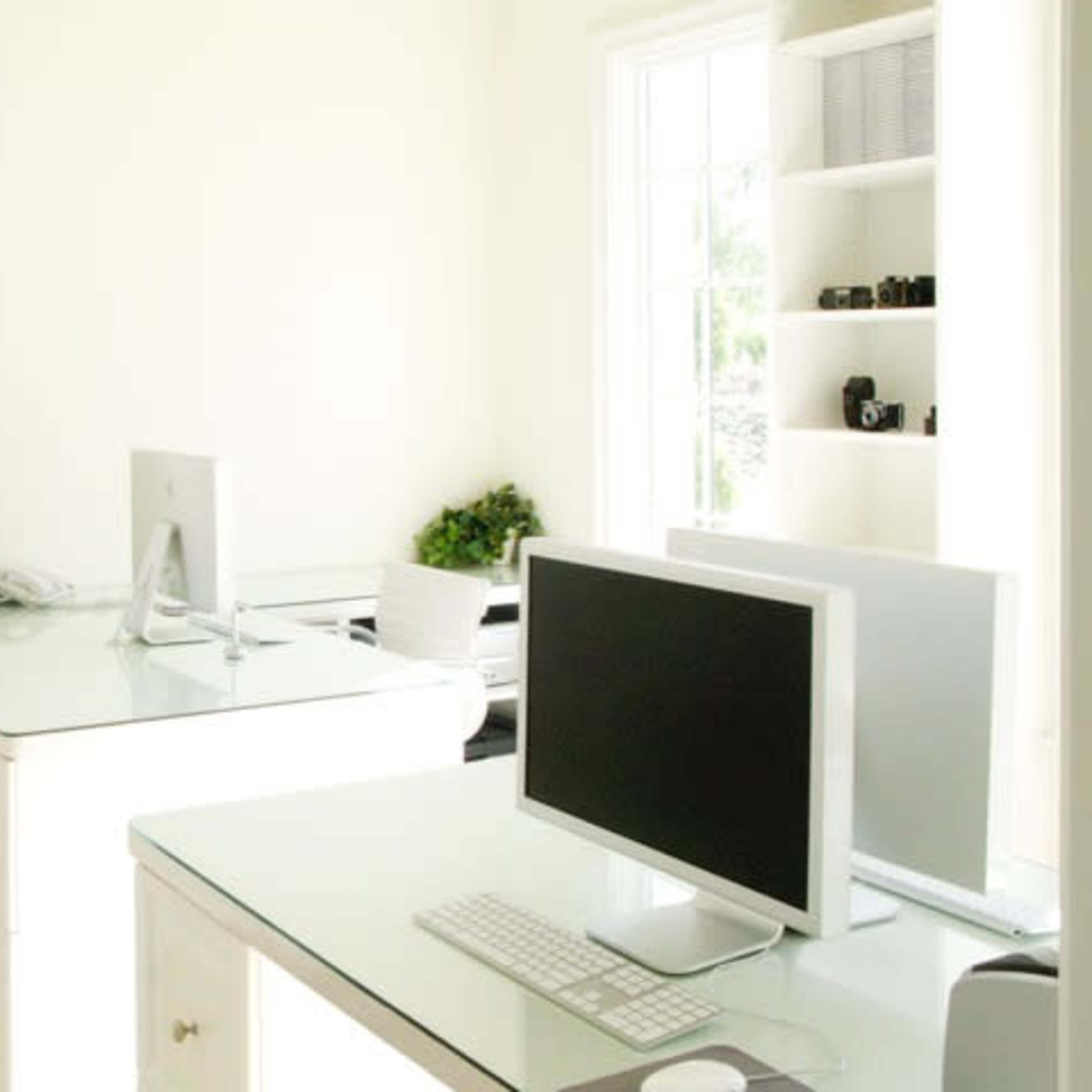 A bright, minimalist office with two glass-topped desks, each featuring a computer and a few decorative items.