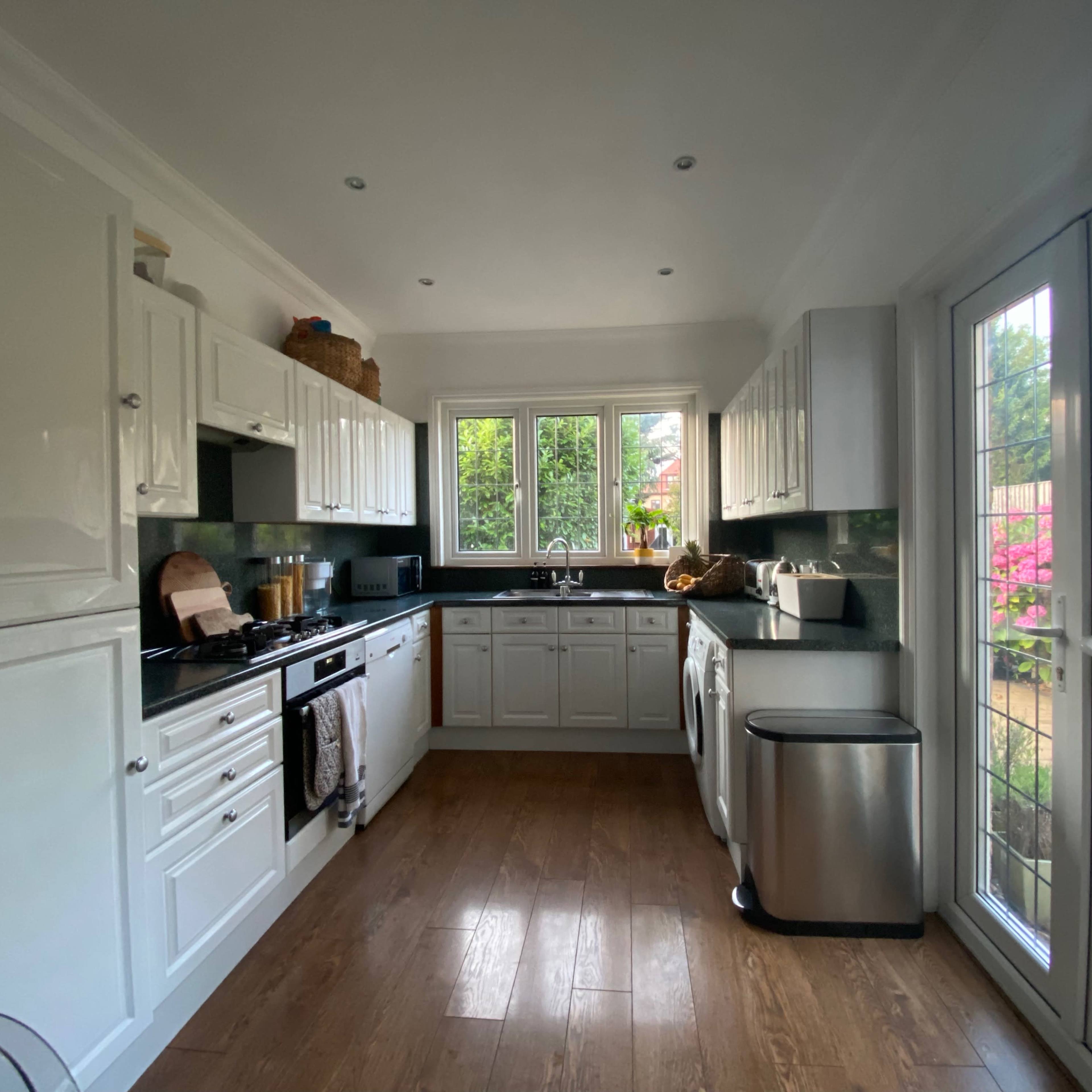 The kitchen features white cabinetry, a black countertop, and large windows overlooking a garden.